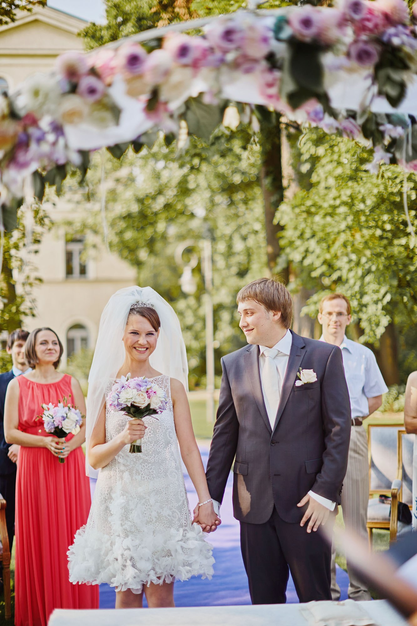 Ludmila smiles after Sergey said 'I do' under the floral arch during their summer wedding at the Chateau Mcely.