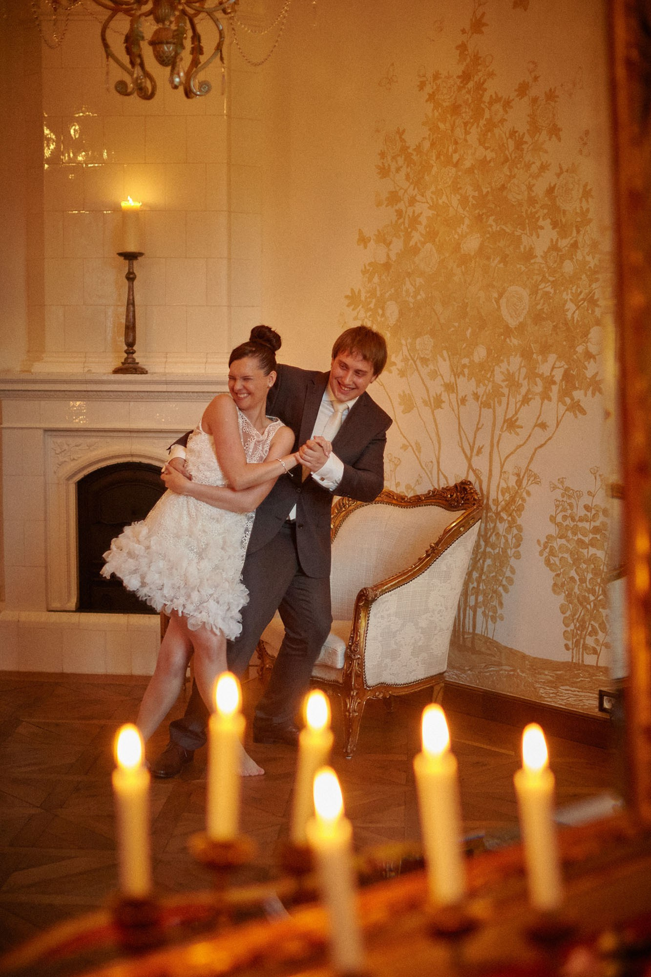 Newlyweds burst into laughter during their hilariously imperfect waltz, captured in a candlelit mirror at the romantic Chateau Mcely.
