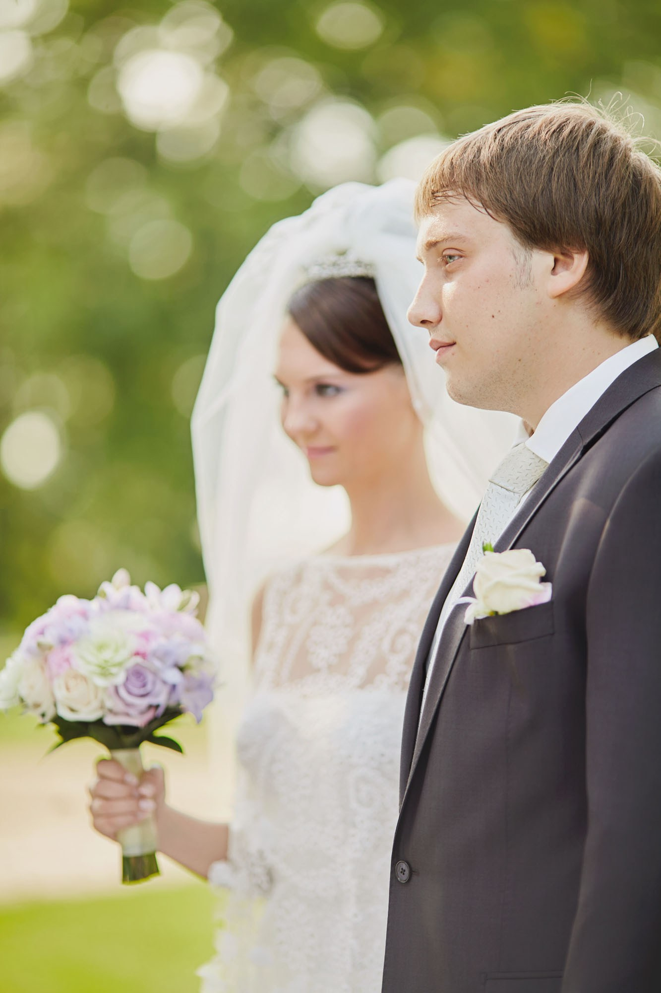 A bride, holding her bouquet, listens intently to the wedding officials during her outdoor garden wedding at a chateau in Czechia.