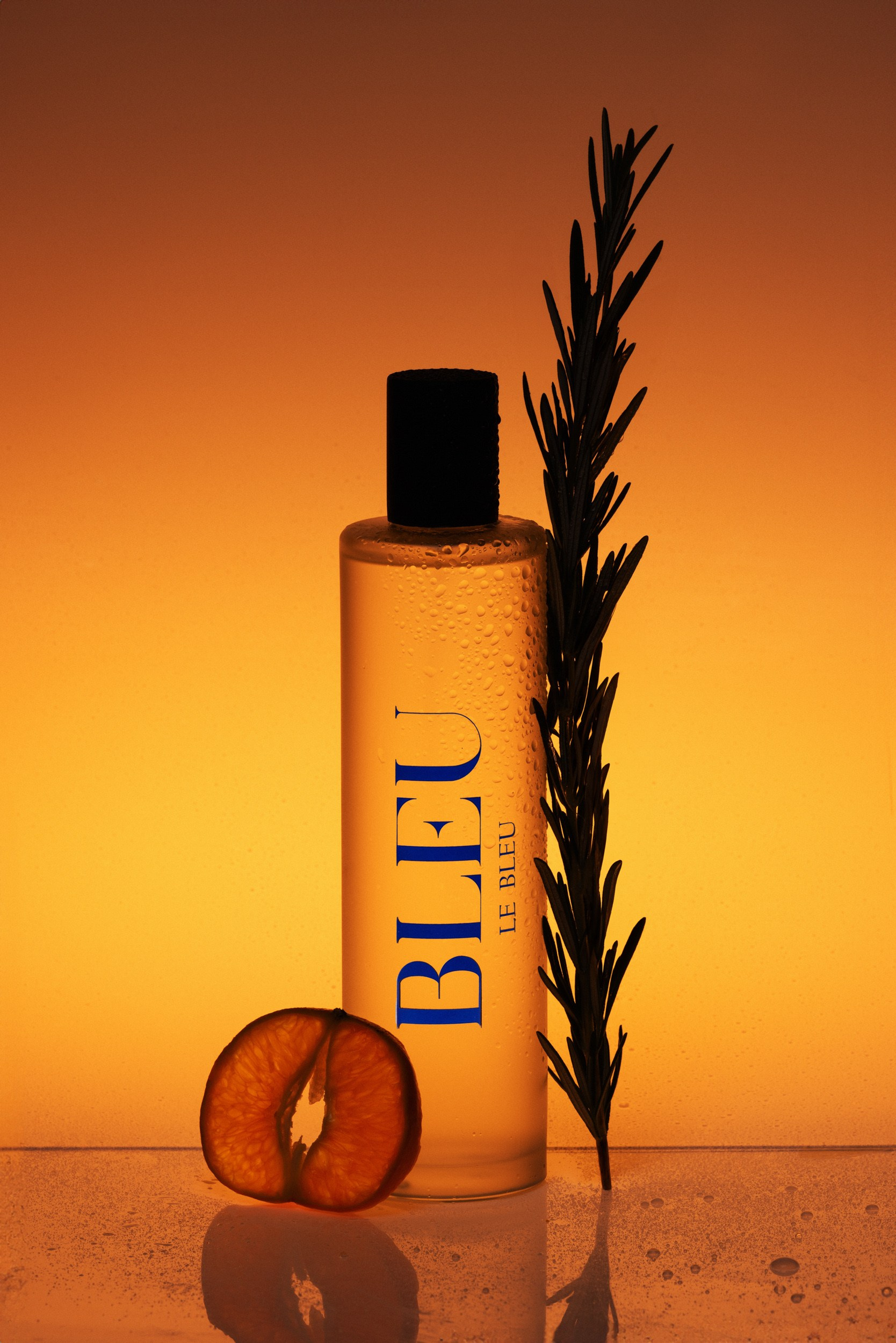 Elegant perfume bottle with a black cap, illuminated by a vibrant amber background, featuring fresh rosemary and citrus elements