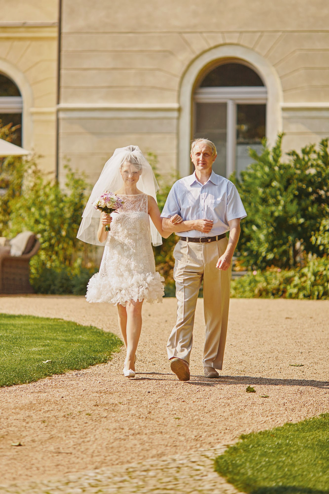 Proud father escorting bride across lawn at Chateau Mcely summer wedding.