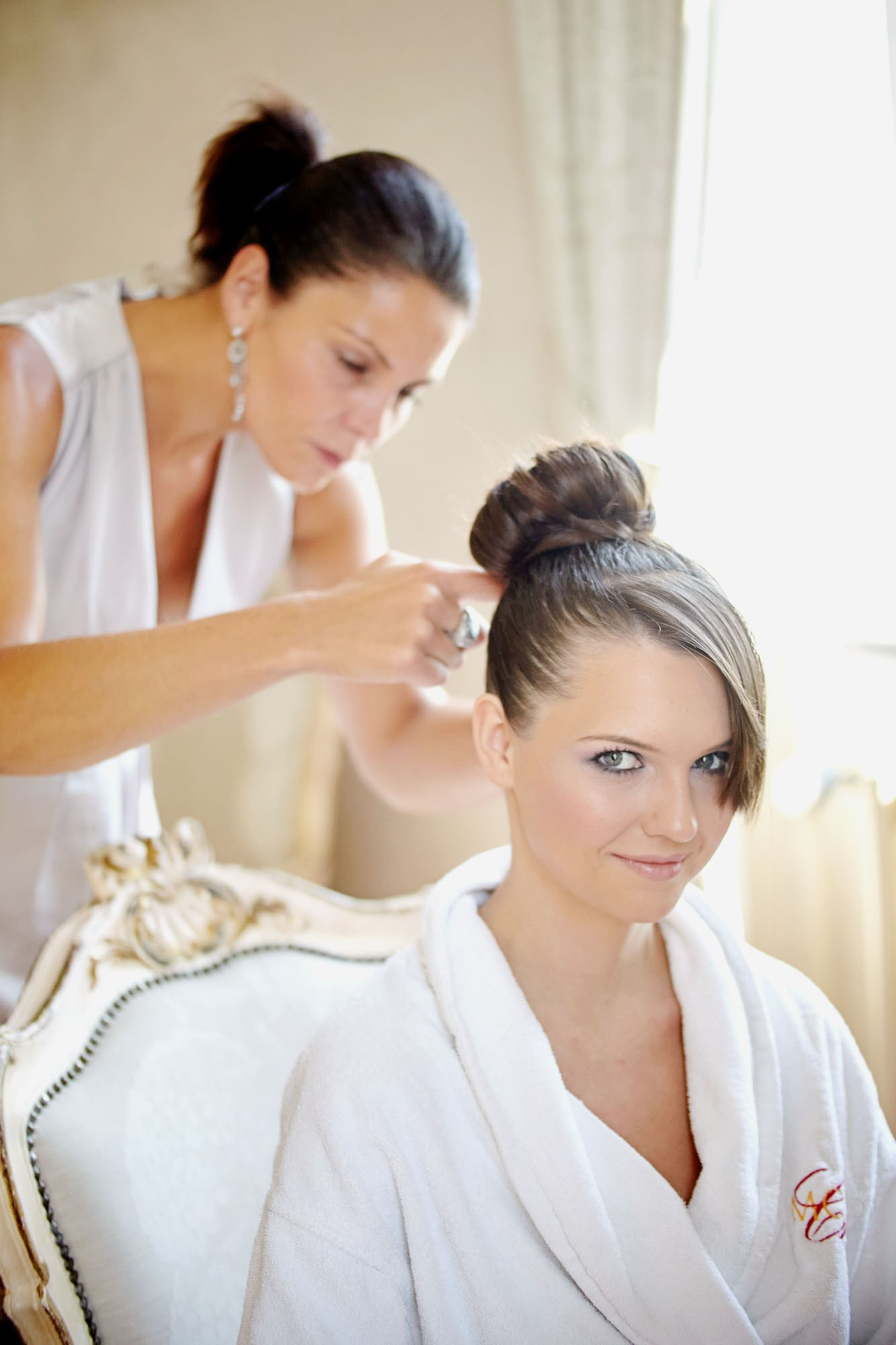 Hair and makeup artist styling the back of the bride's hair during bridal prep.