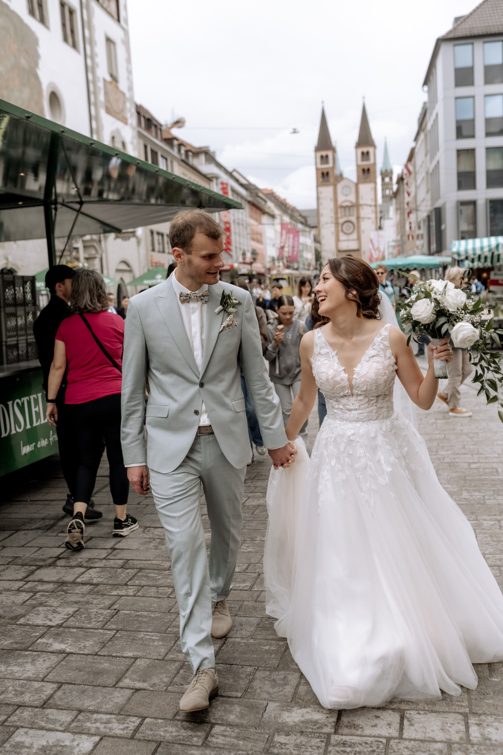 Das Brautpaar spaziert verliebt über die Alte Mainbrücke in Würzburg. Im Hintergrund sind die Festung Marienberg und der Main zu sehen, goldenes Abendlicht taucht die Szene in Wärme.