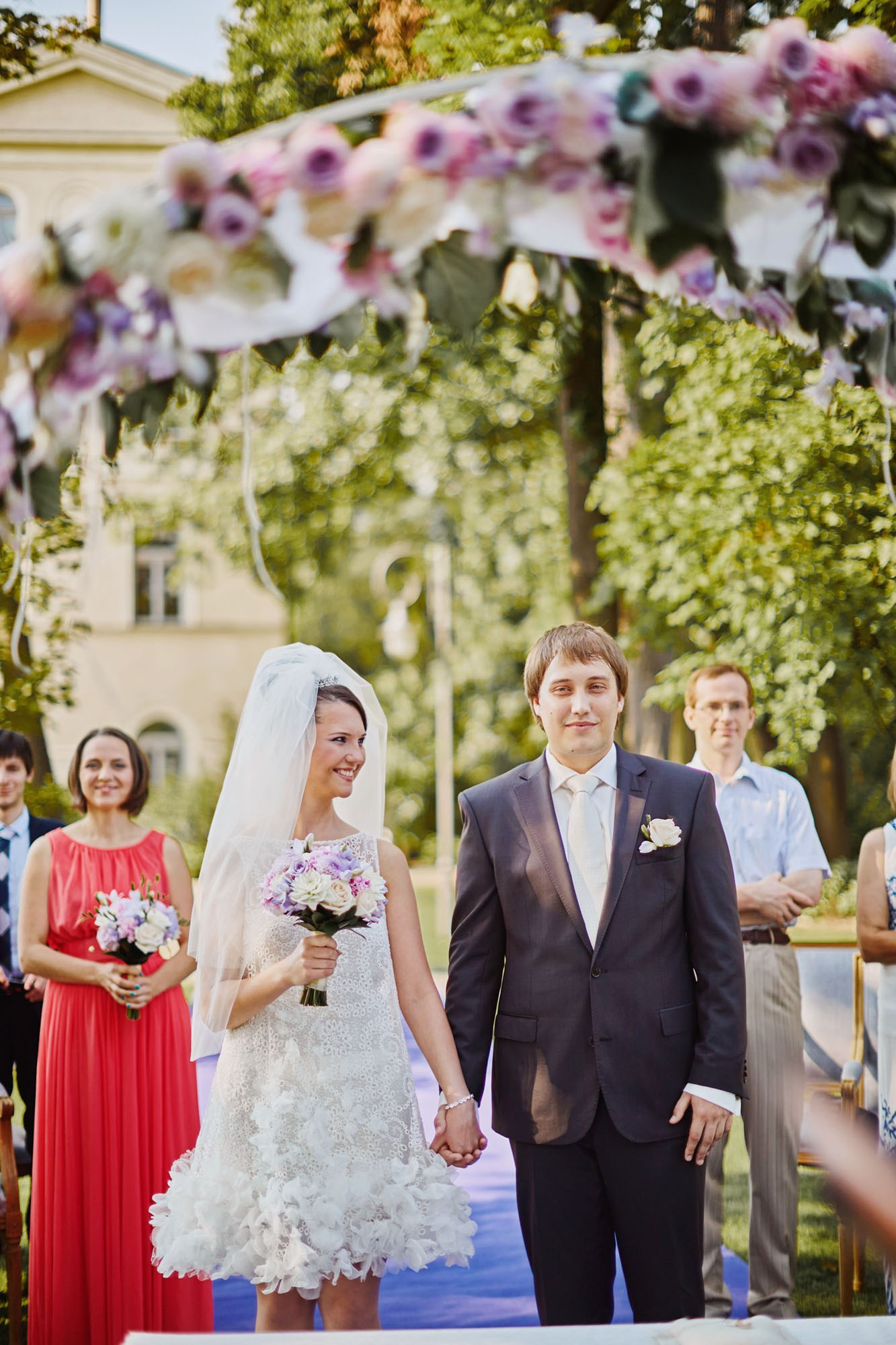 Ludmila smiling after 'I do' under the floral arch during their summer wedding at the Chateau Mcely.