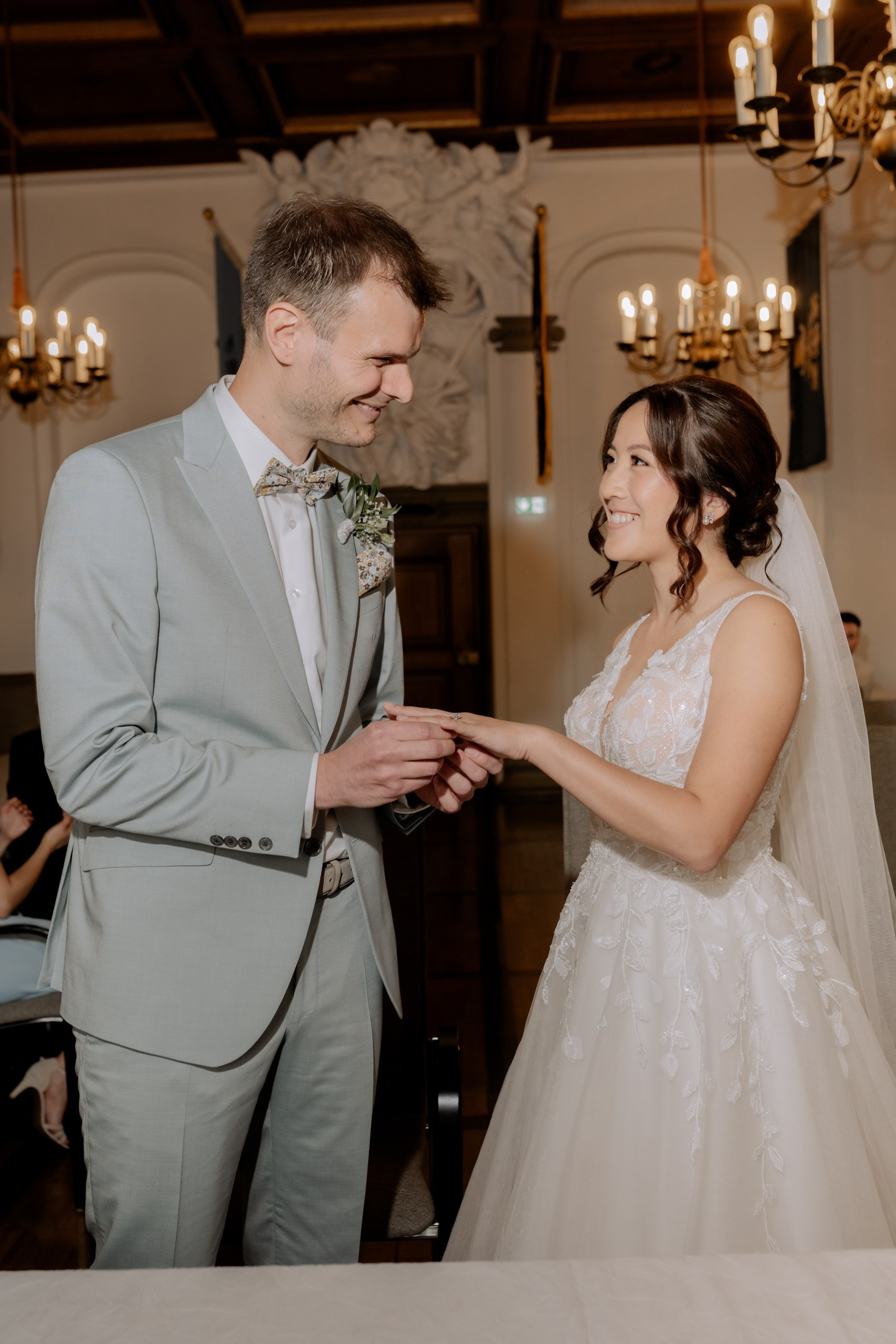 Blick auf die Braut, wie sie dem Bräutigam liebevoll in die Augen sieht. Im Hintergrund verschwommen sanfte Steinwände des Standesamts.