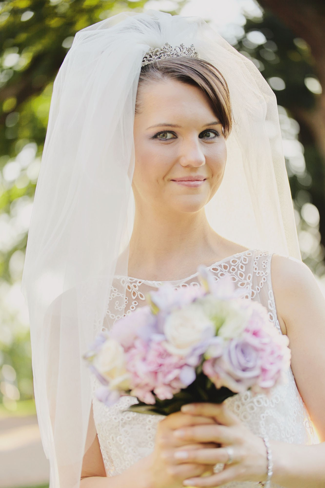 A joyful bride beams for the camera, bouquet in hand, on the lush grounds of Chateau Mcely in Czechia post-wedding.