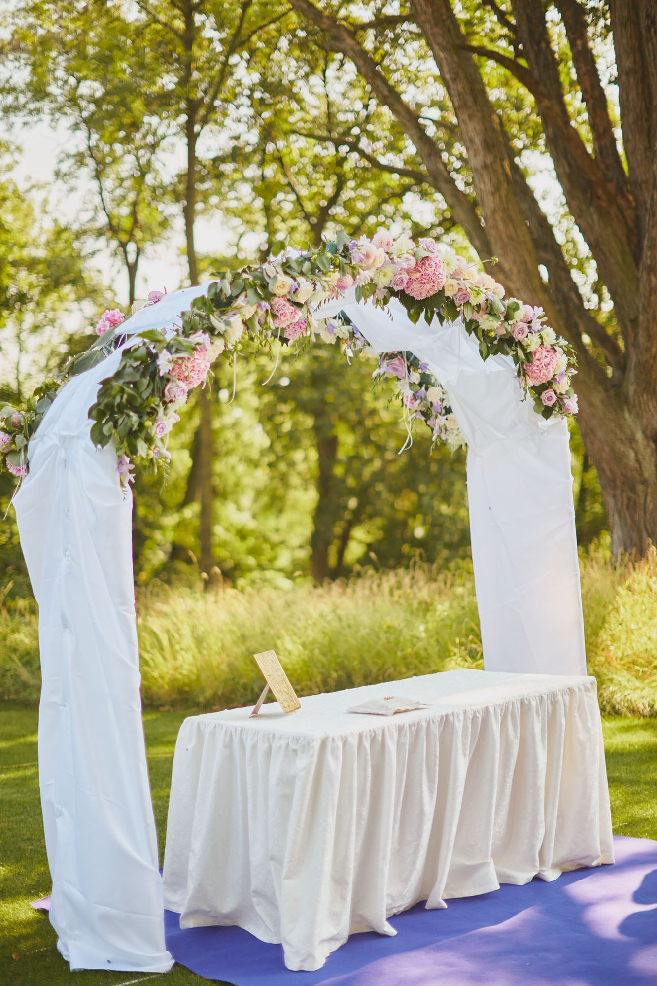 Sunlit floral arch with a French blue carpet on the scenic grounds of a historic Czech chateau.