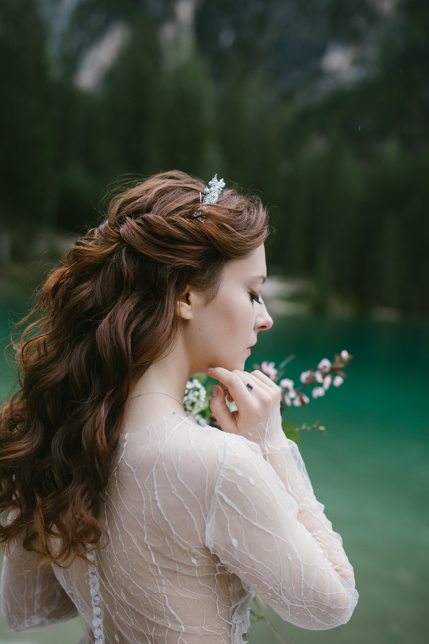 Braut im Spitzenkleid mit Blumenstrauß am Seeufer