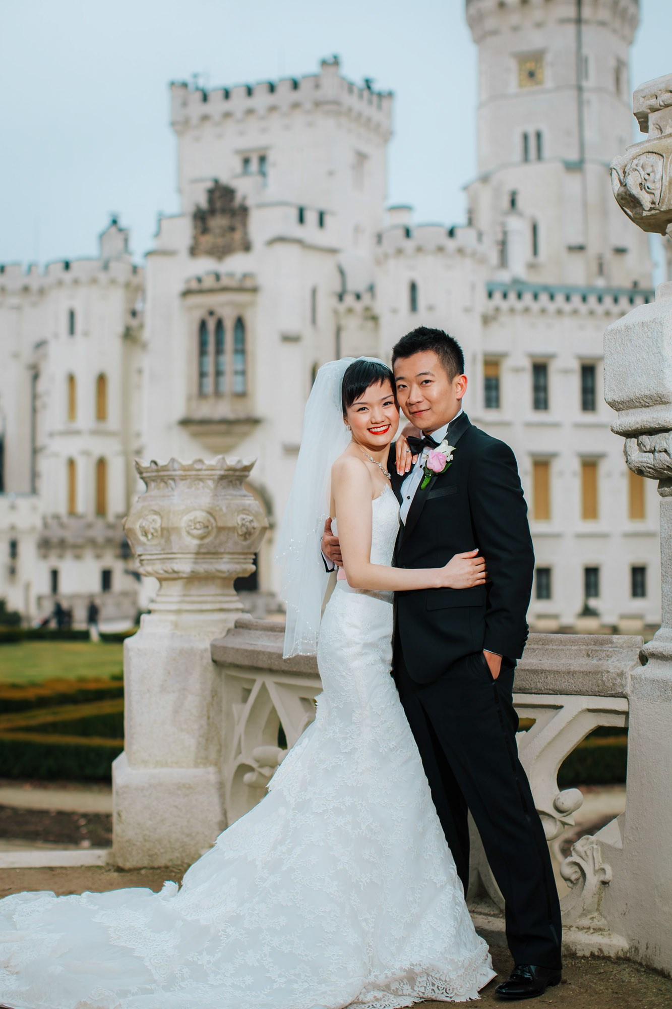 A radiant Hong Kong bride and her groom pose for a photo against hte backdrop of the famed Castle Hluboka during their wedding day in Czechia.