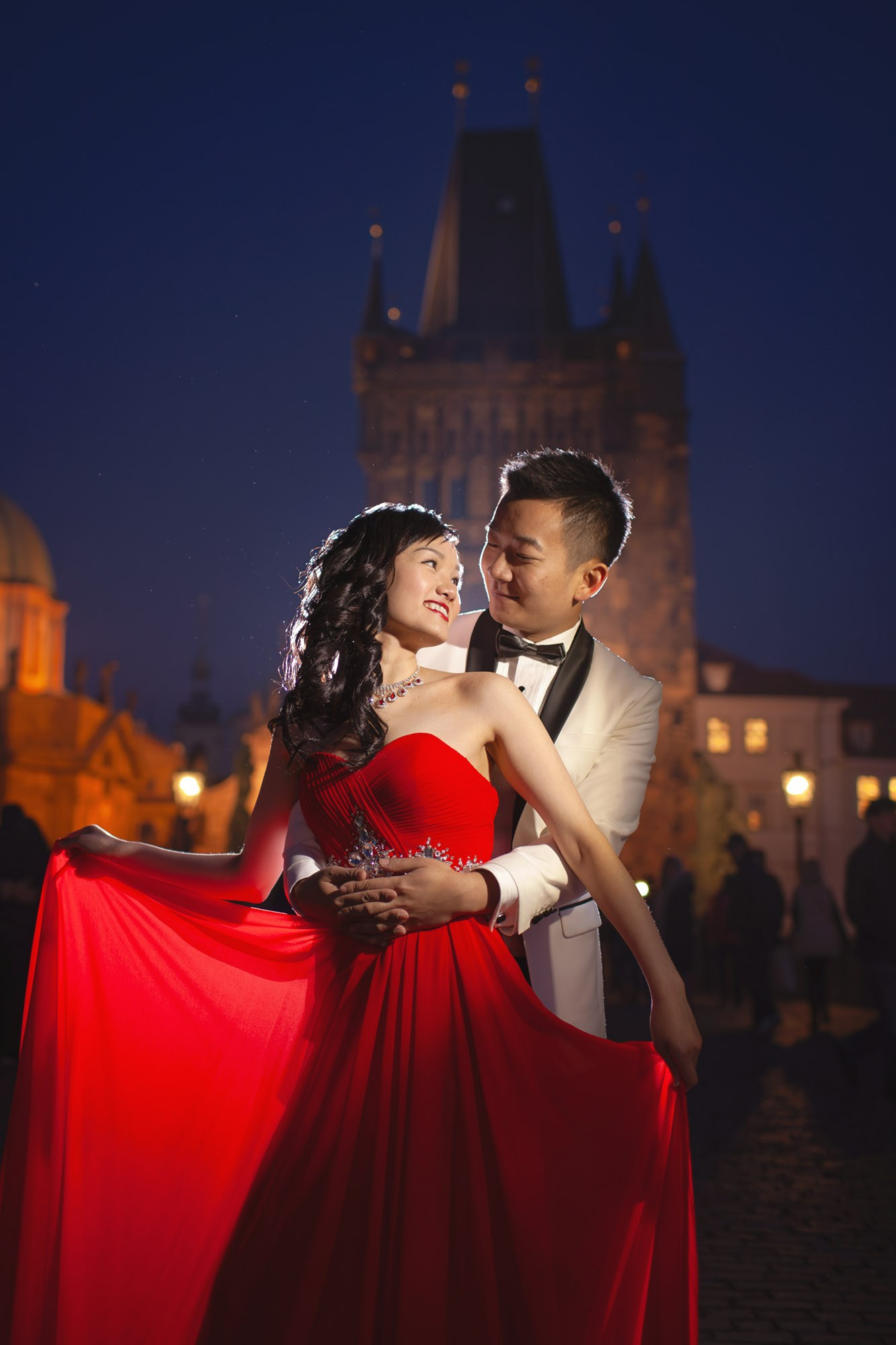 A stylishly dressed Hong Kong couple poses for a portrait on the historic Charles Bridge at night.