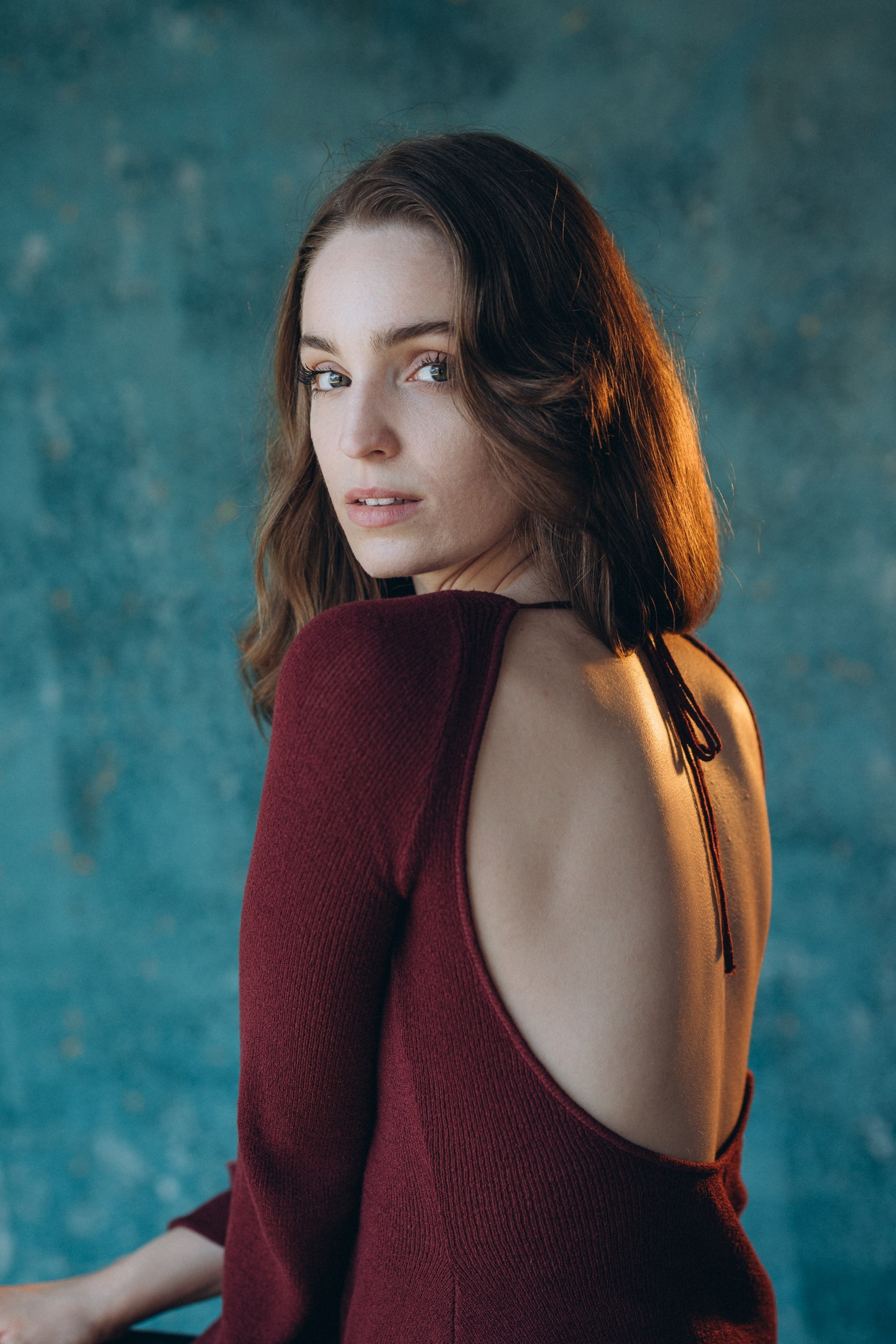 Actor headshot of a woman in a sleeveless burgundy top, looking to the side with dramatic lighting