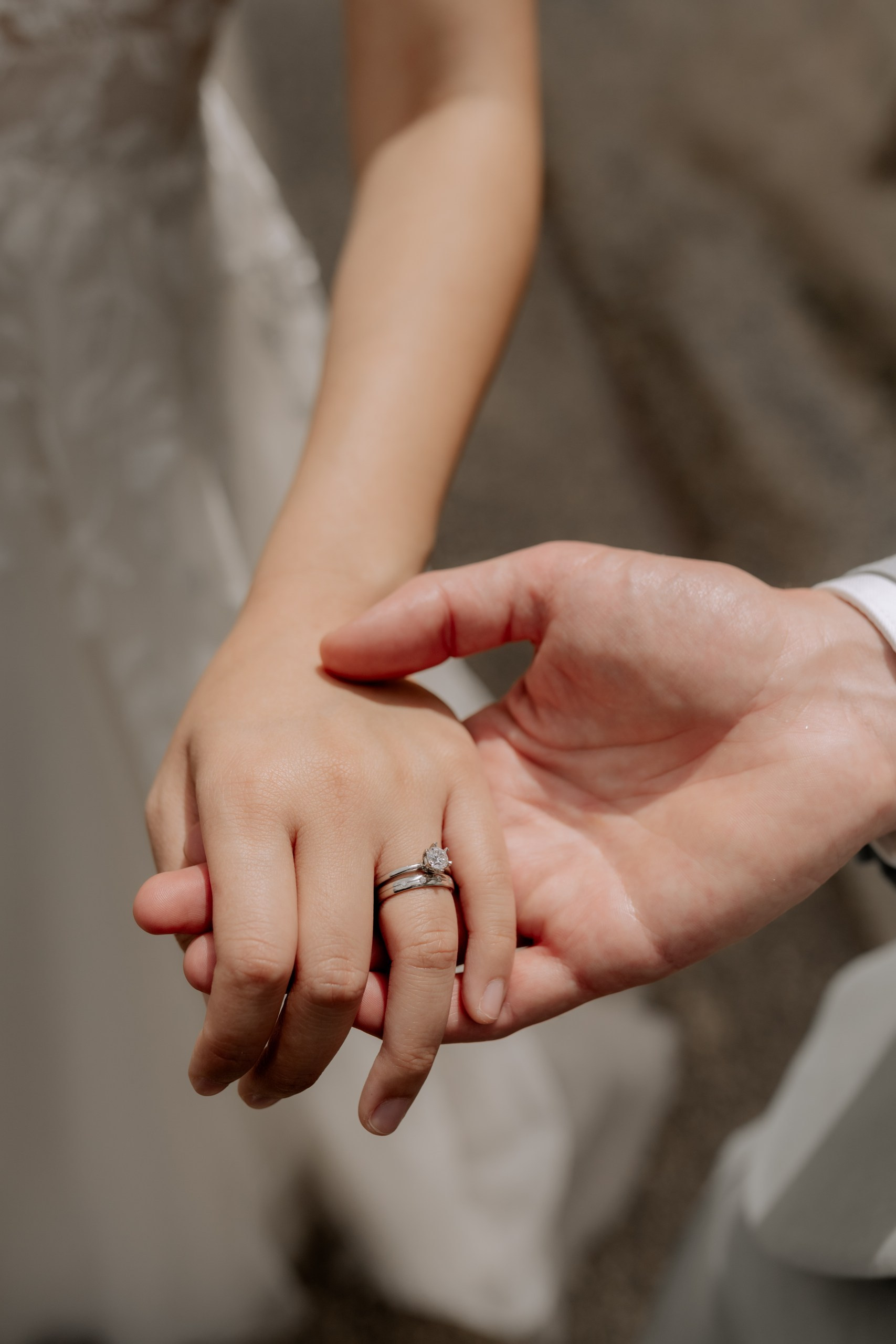 Die Hände des Brautpaars auf der alten Brüstung aus Stein, Eheringe im Fokus – dahinter unscharf der Fluss und das Abendlicht.