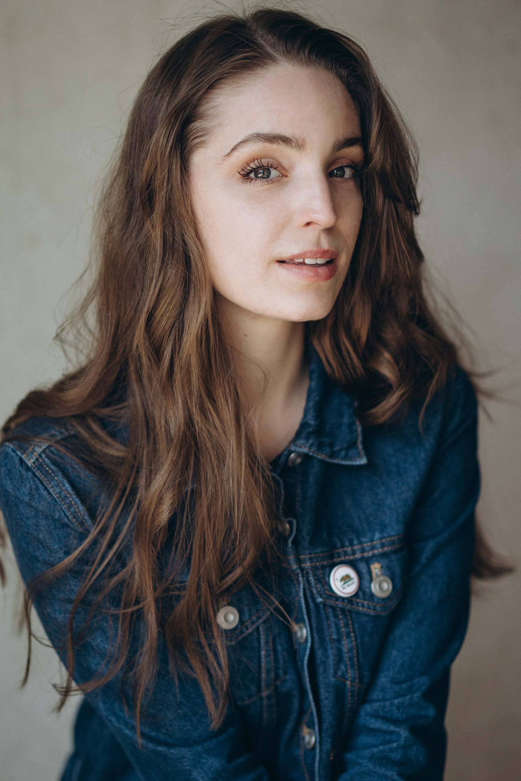 Actor headshot of a woman with long wavy hair wearing a denim jacket, looking confidently at the camera