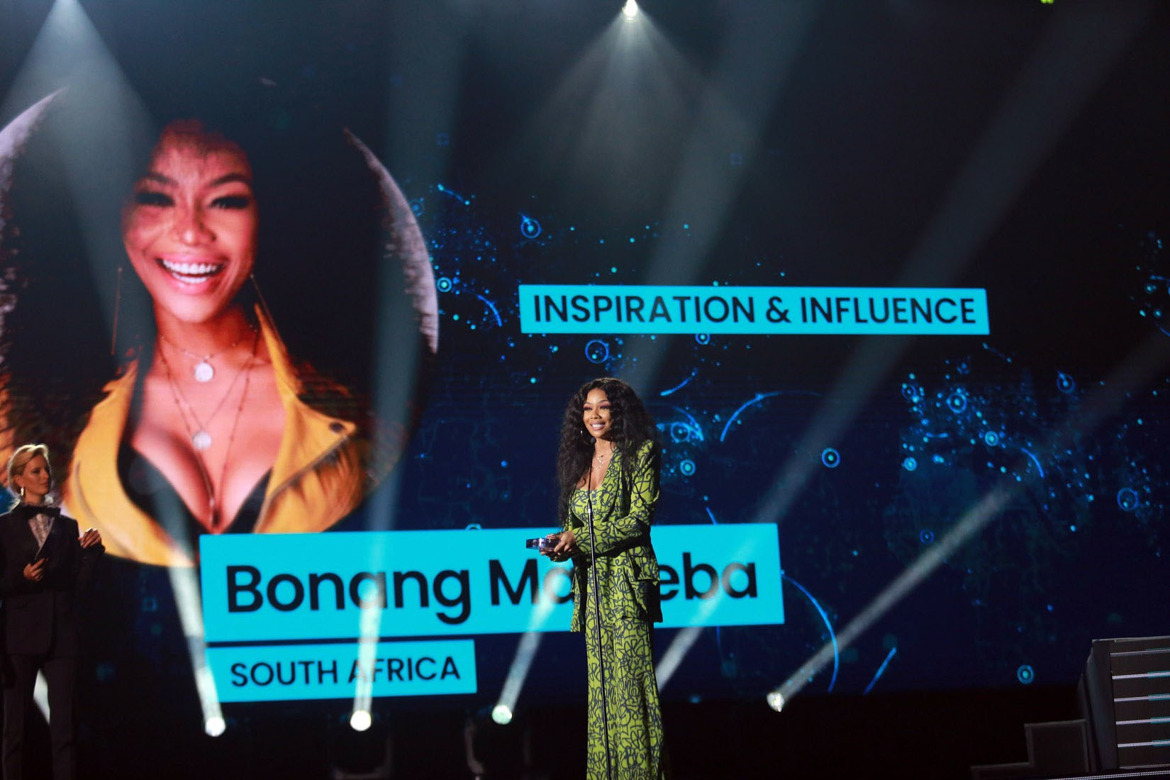 Bonang Matheba holds up her trophy, smiling confidently towards the camera after winning the prestigious Inspiration & Influence Award at the 2019 Global Social Awards. The live-streamed event, held at the Forum in Prague, celebrated top social media influencers from around the world, recognizing their impact and reach. This moment highlights Bonang’s achievement as a leading African media personality on an international stage.