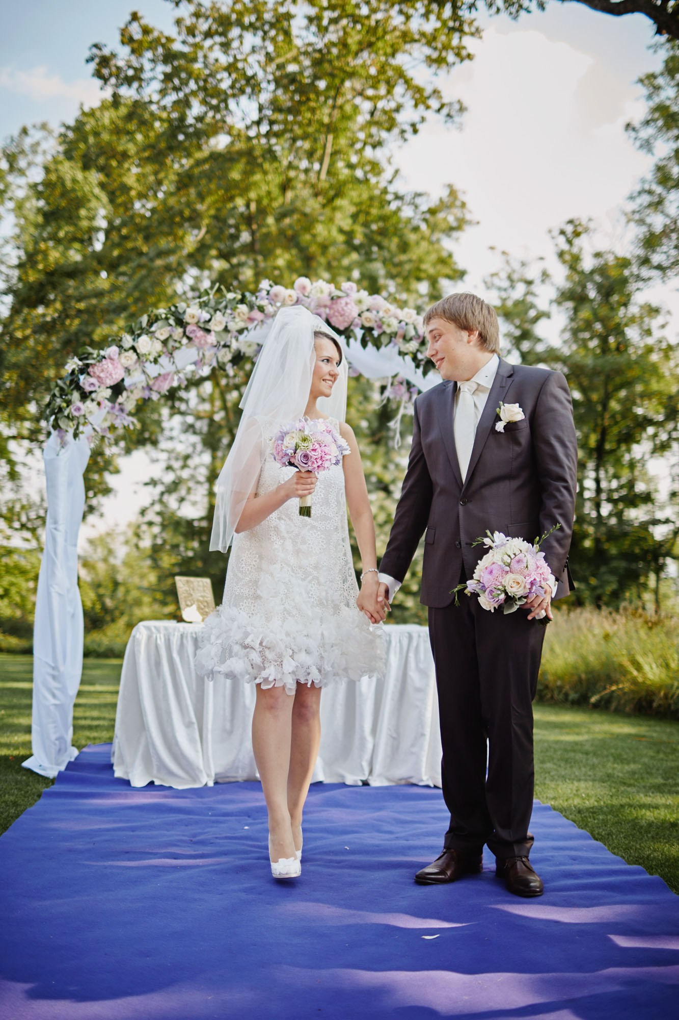 Smiling newlyweds on French Blue carpet post-outdoor wedding.