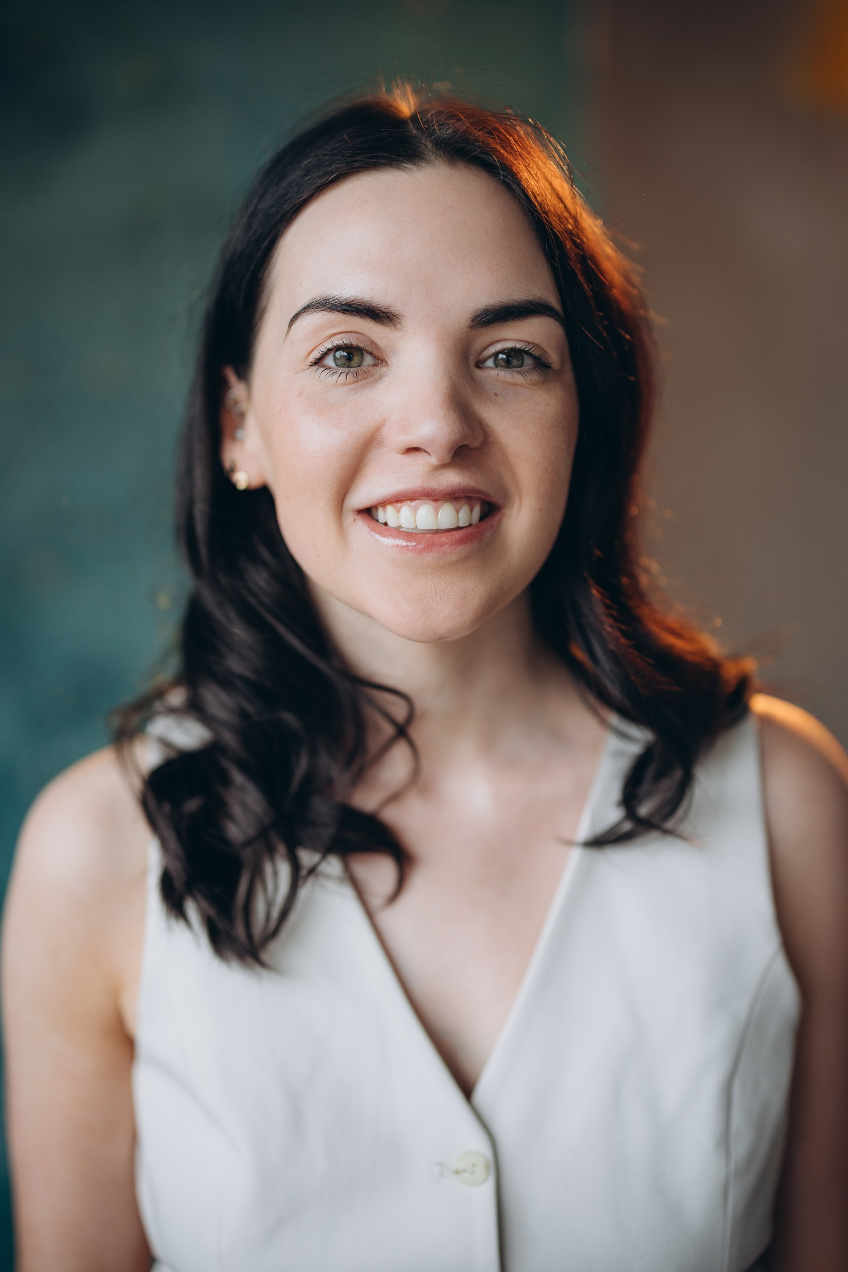 Actor headshot of a happy woman with dark hair in a white blouse, smiling and facing the camera