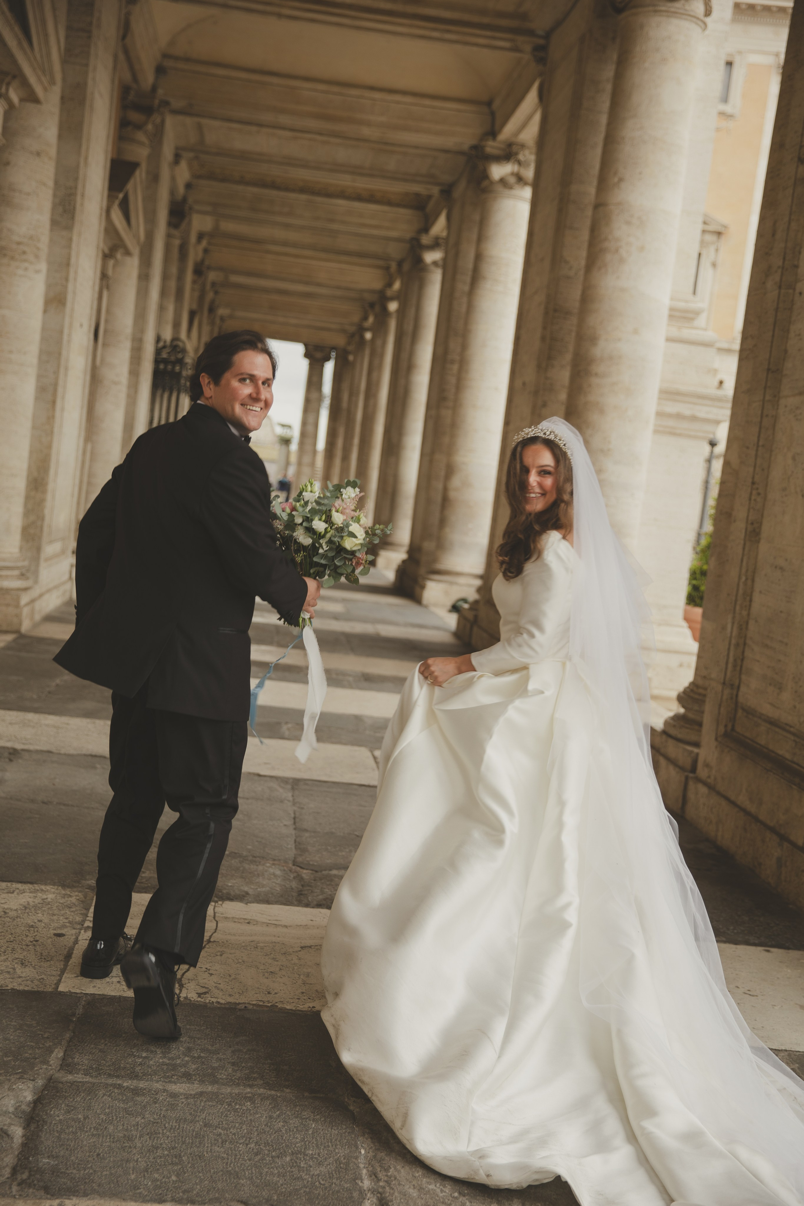 Newly married couple running joyfully through the arcades of Piazza del Campidoglio in Rome.