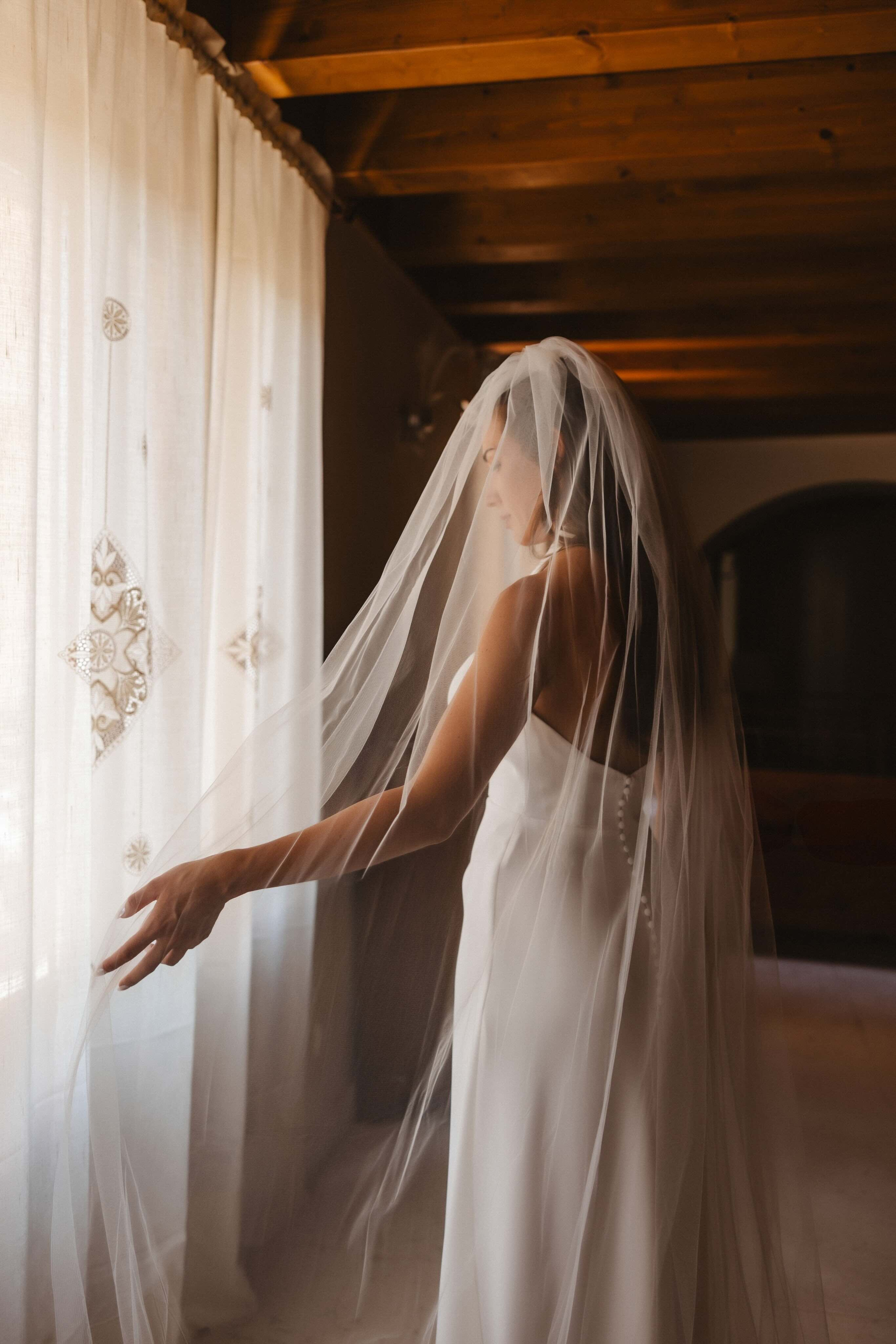 Noiva elegante ao sol a ajustar o véu durante um casamento num palácio em Itália