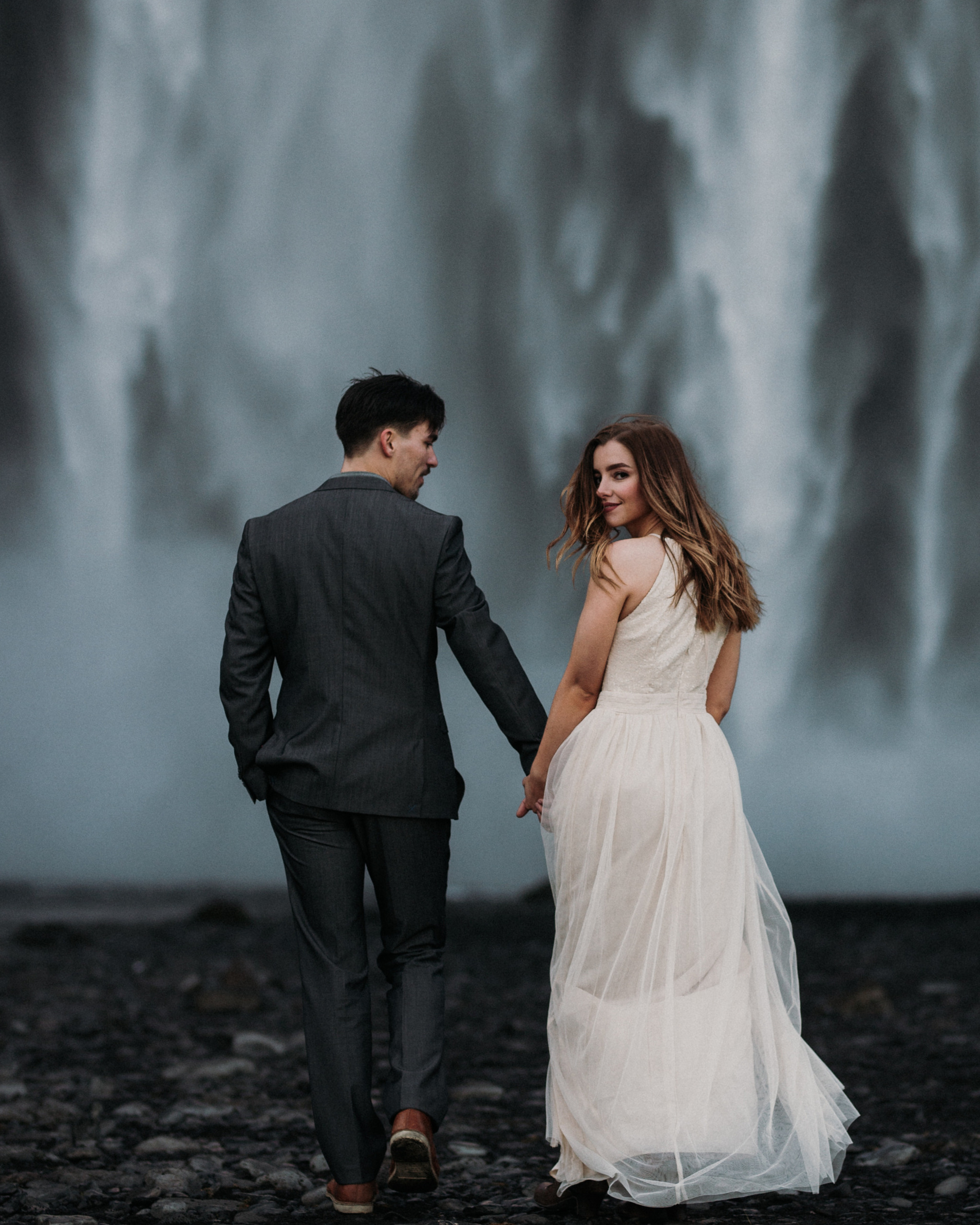 Romantic wedding couple embracing against the backdrop of a stunning Icelandic waterfall.