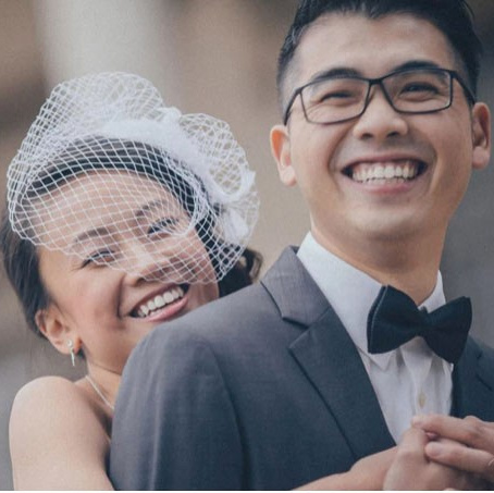 Red-haired bride holding her flowing veil aloft smiles seductively to her bouquet holding groom as he leans back against a railing in appreciation at the Vrtba Garden in Prague. 
