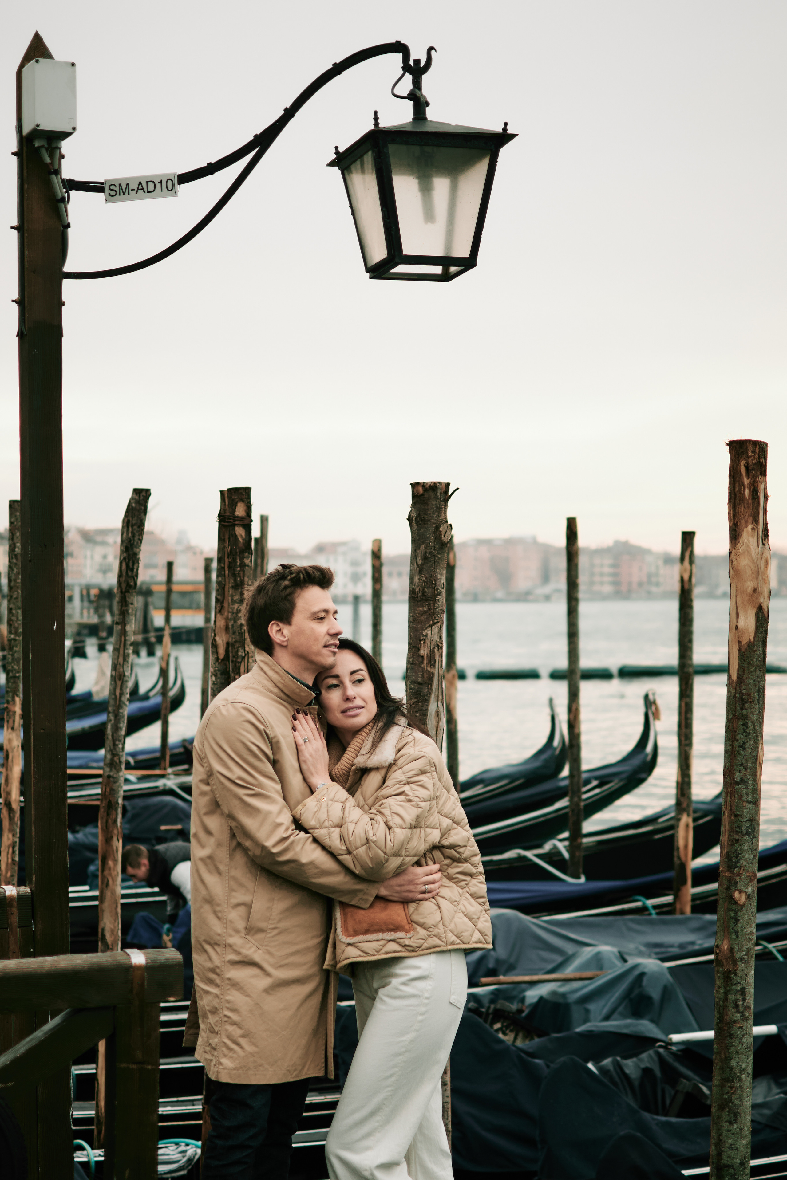 A couple stands on the edge of a beautiful lagoon in the background. The warm, golden light of the sun sets behind them, casting a romantic glow over the scene.