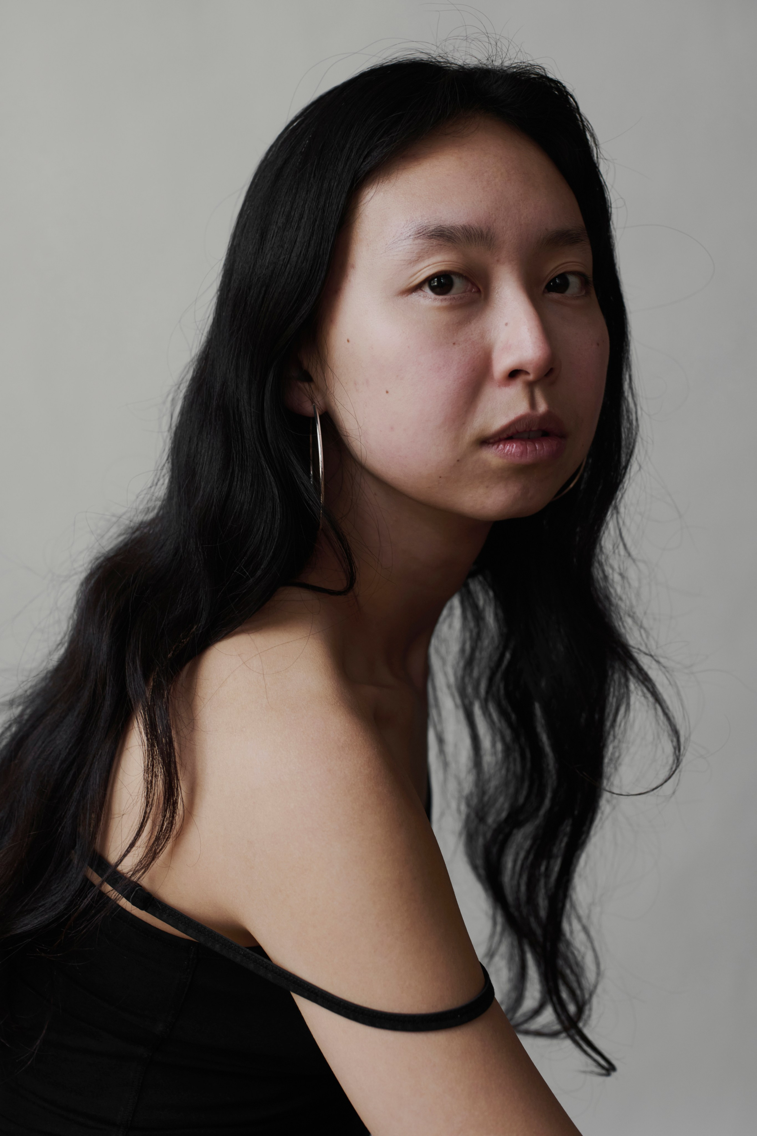 Artistieke portretfotografie van een jonge vrouw met lang donker haar en grote oorbellen, gefotografeerd tegen een neutrale achtergrond in Amsterdam.