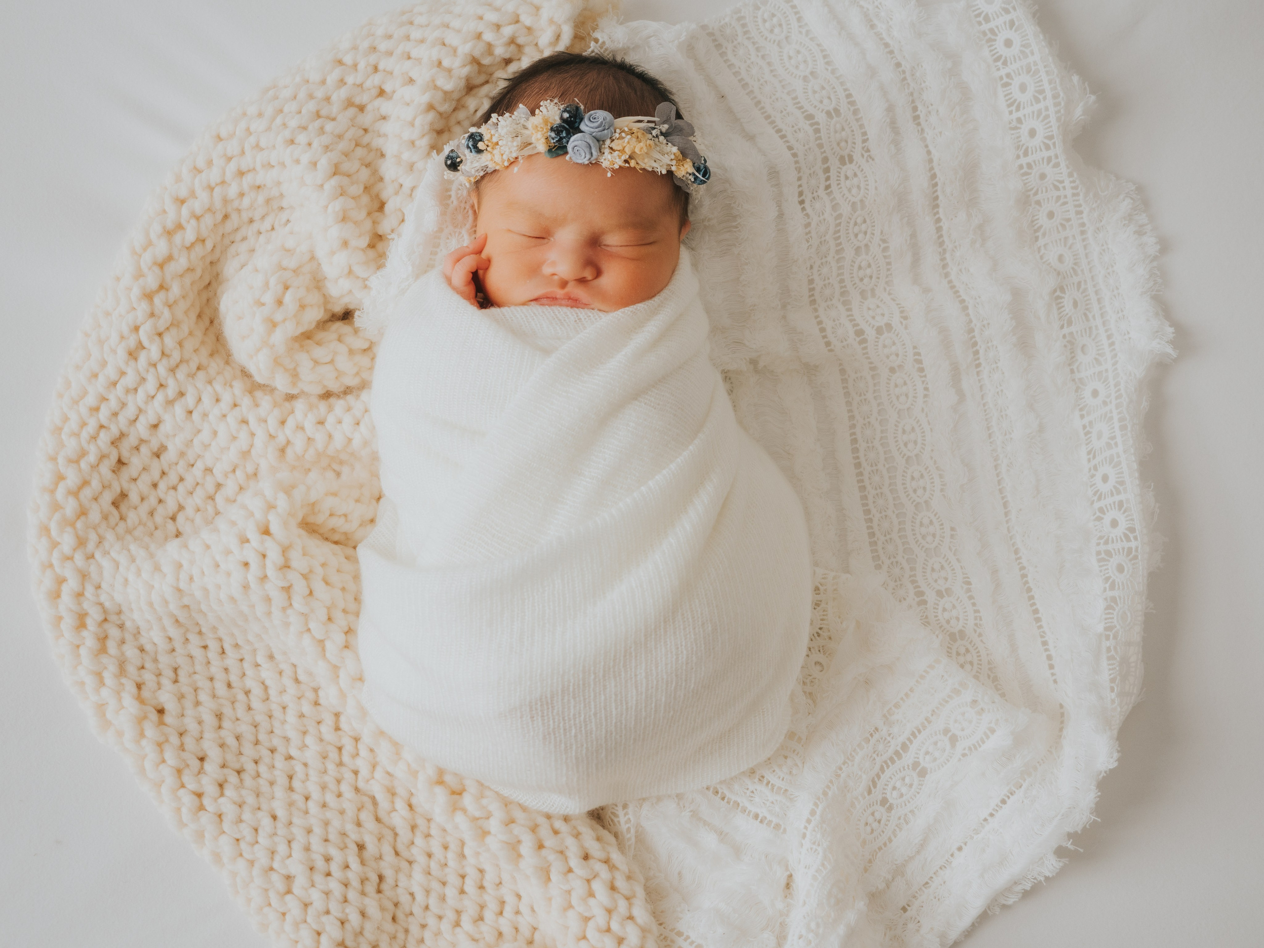Bébé endormi emmailloté dans des couvertures blanches et crème.