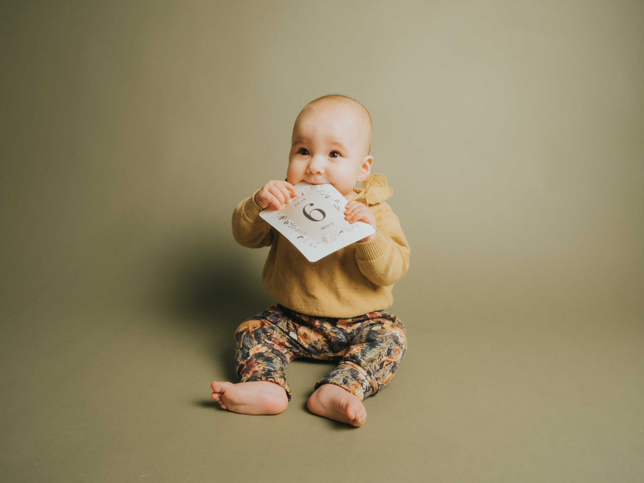 Petite fille sur fond couleur vert avec pastille de 6 mois dans la bouche.