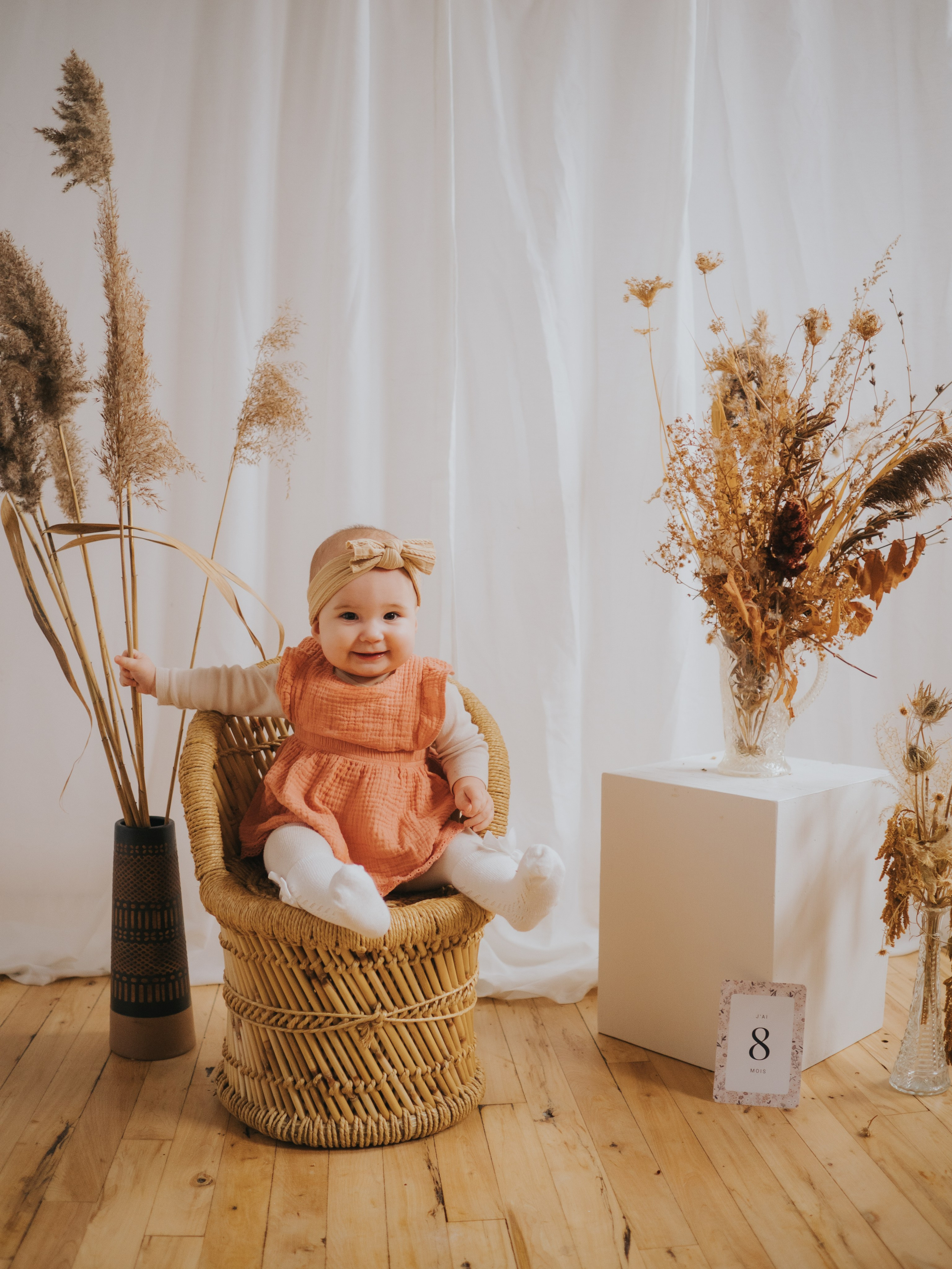 Bébé assise sur chaise en rotin avec pastille de 8 mois à côté.
