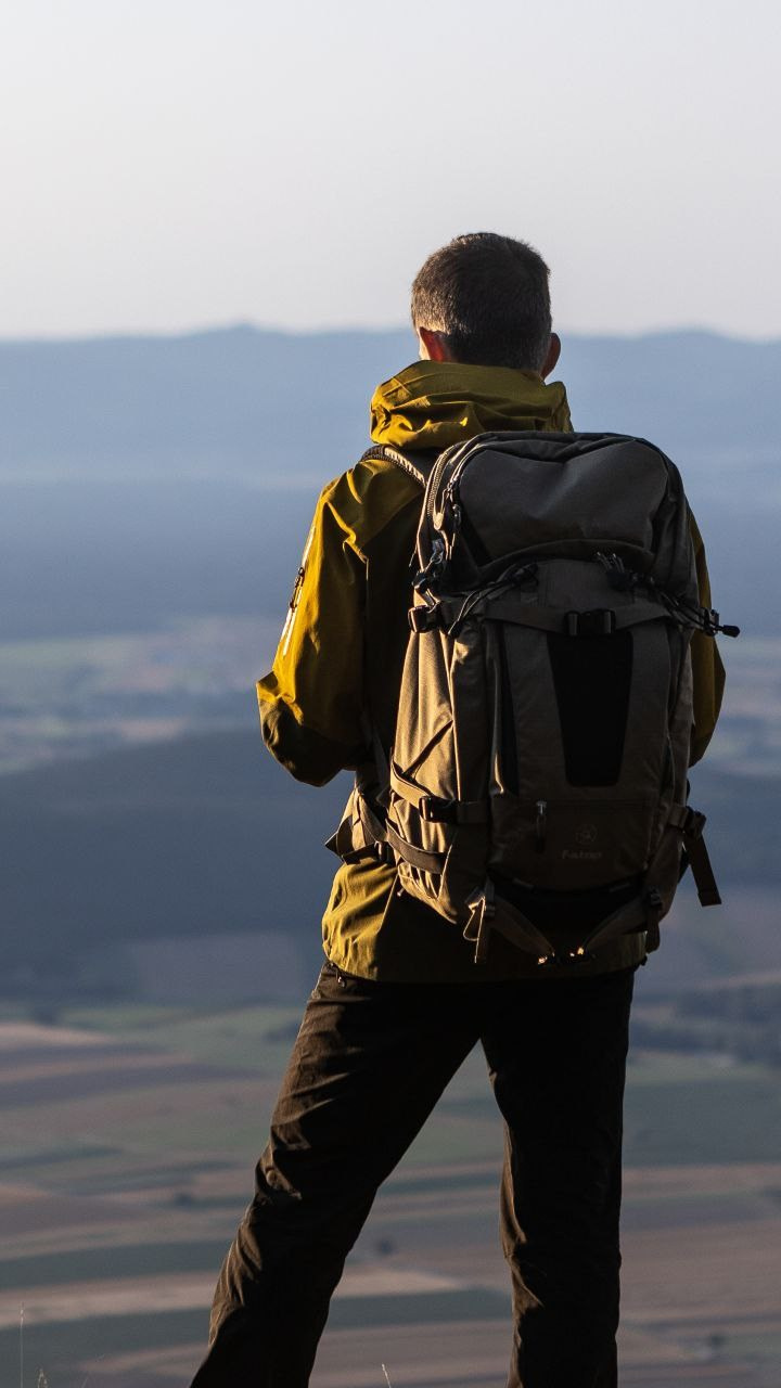 Юрий Меркулов пейзажный фотограф оператор-постановщие с рюкзаком F-Stop Gear Tilopa 50L смотрит в даль на пейзаж на рассвете ранним утром.