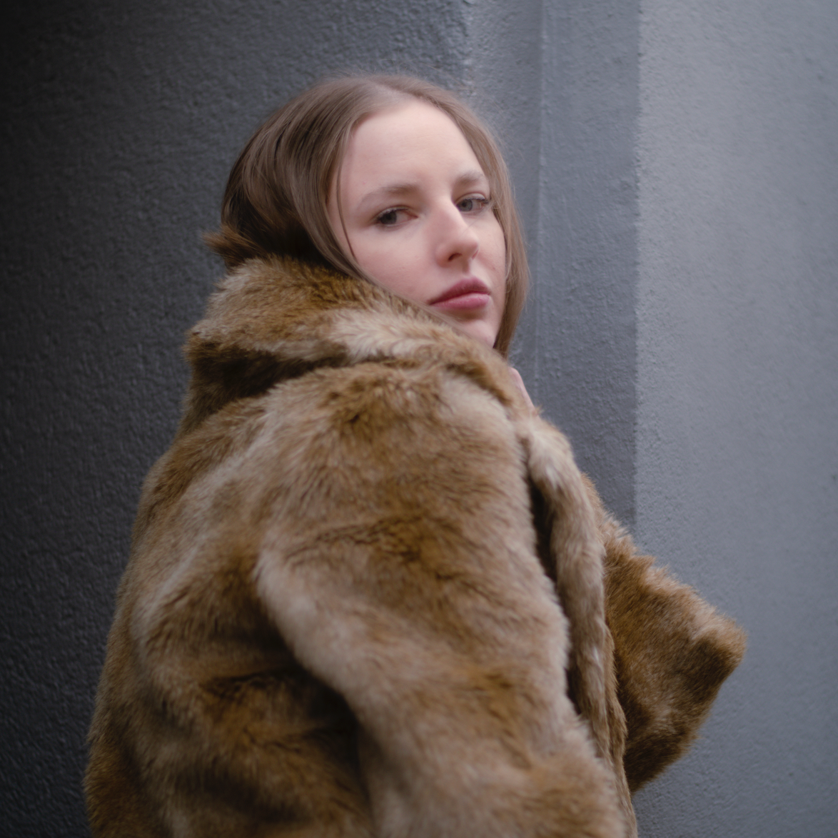 Porträt einer jungen Frau im Pelzmantel mit dunkelblonden Haaren, blauen Augen vor einem blau-grauen Hintergrund