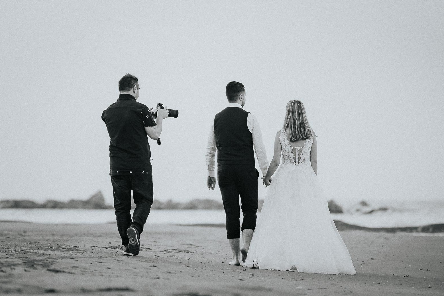 Sposi in corsa davanti al Colosseo in bianco e nero, immagine dinamica e gioiosa che cattura lo spirito e la felicità del loro giorno speciale, un ricordo indimenticabile fissato dall'obiettivo di un fotografo esperto in matrimoni.