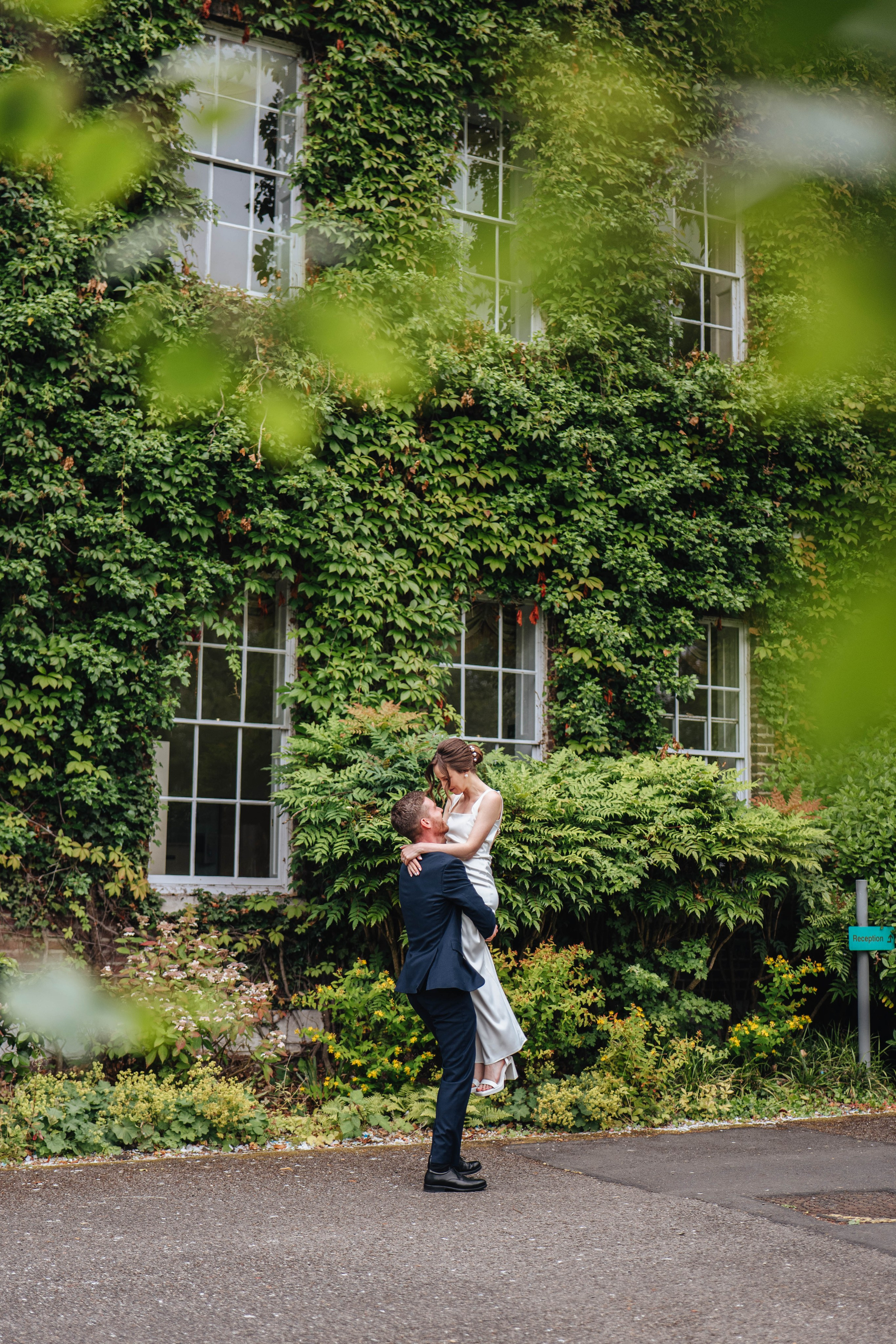 groom lifts and holds the bride on the greenish background