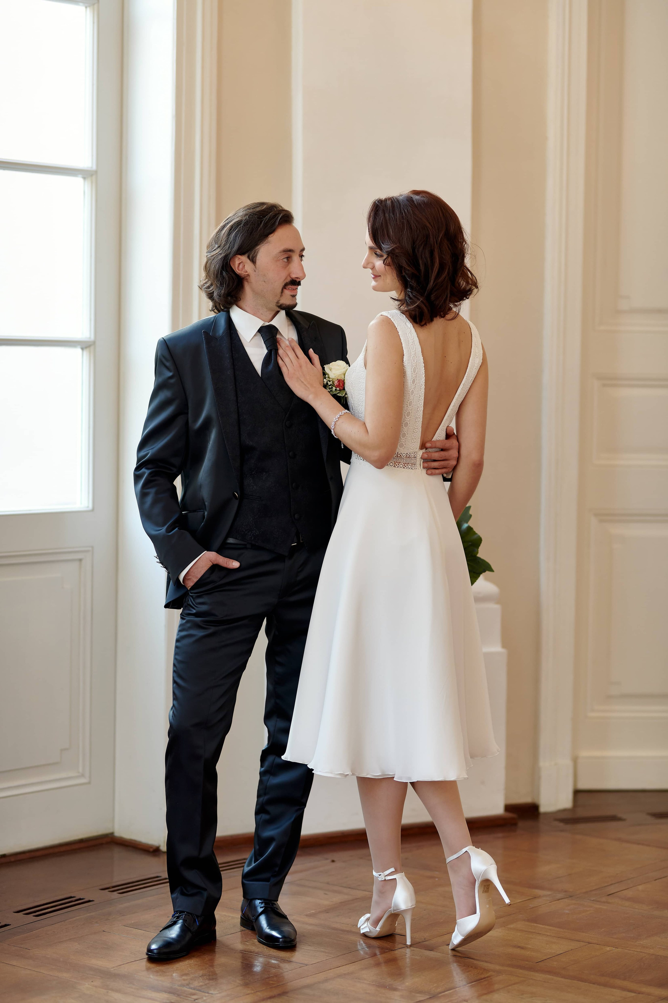 Alexej & Katja in der lichtdurchfluteten Villa Eugenia – ein stiller, eleganter Moment vor der weißen Fensterfront ihrer Trauung.