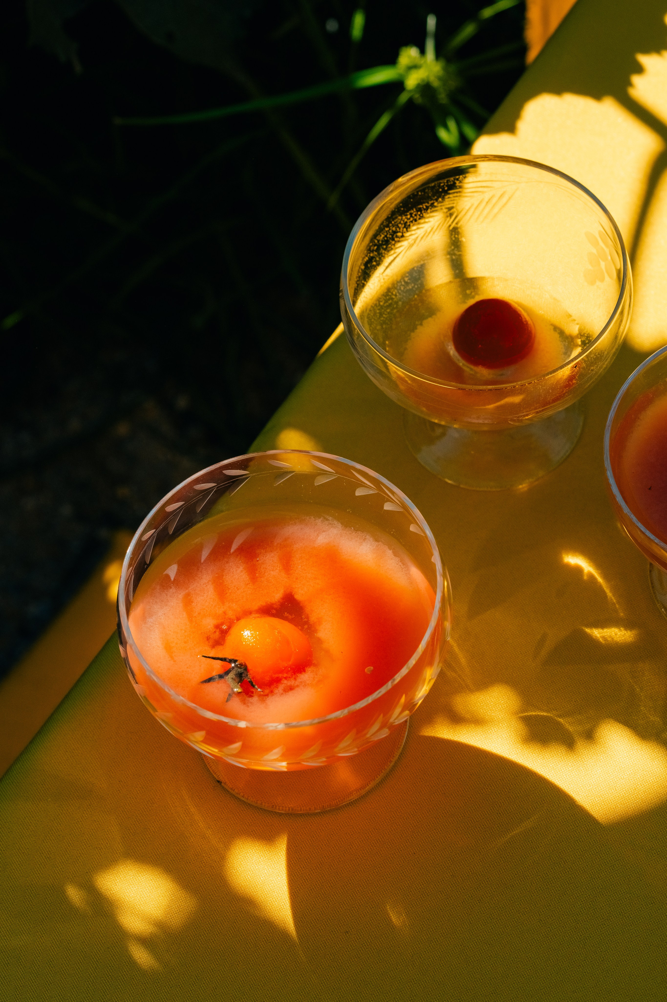 Cocktail de tomate servido em copos com luz e sombras naturais. Uma imagem vibrante de um cocktail de tomate servido em copos transparentes, com tomates cereja a flutuar no topo, sobre um fundo amarelo com sombras divertidas e reflexos de luz.