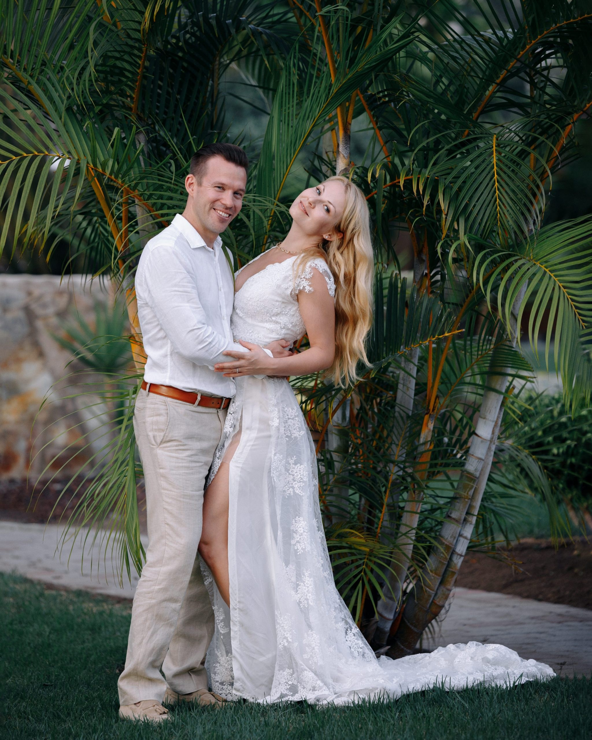A bride and groom posing in front of a palm tree.