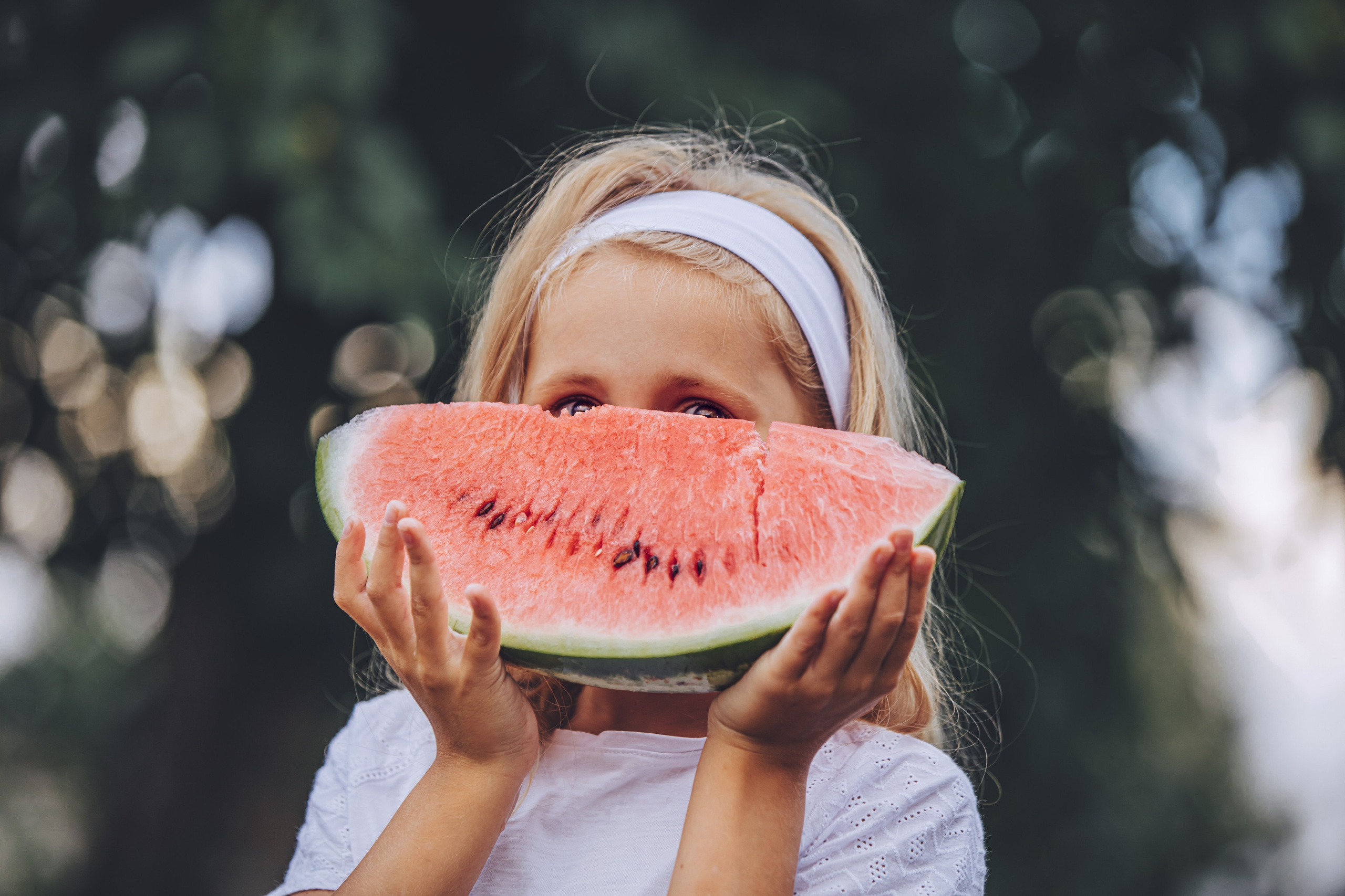 Fillette joyeuse cachant son sourire derrière une grande tranche de pastèque en été