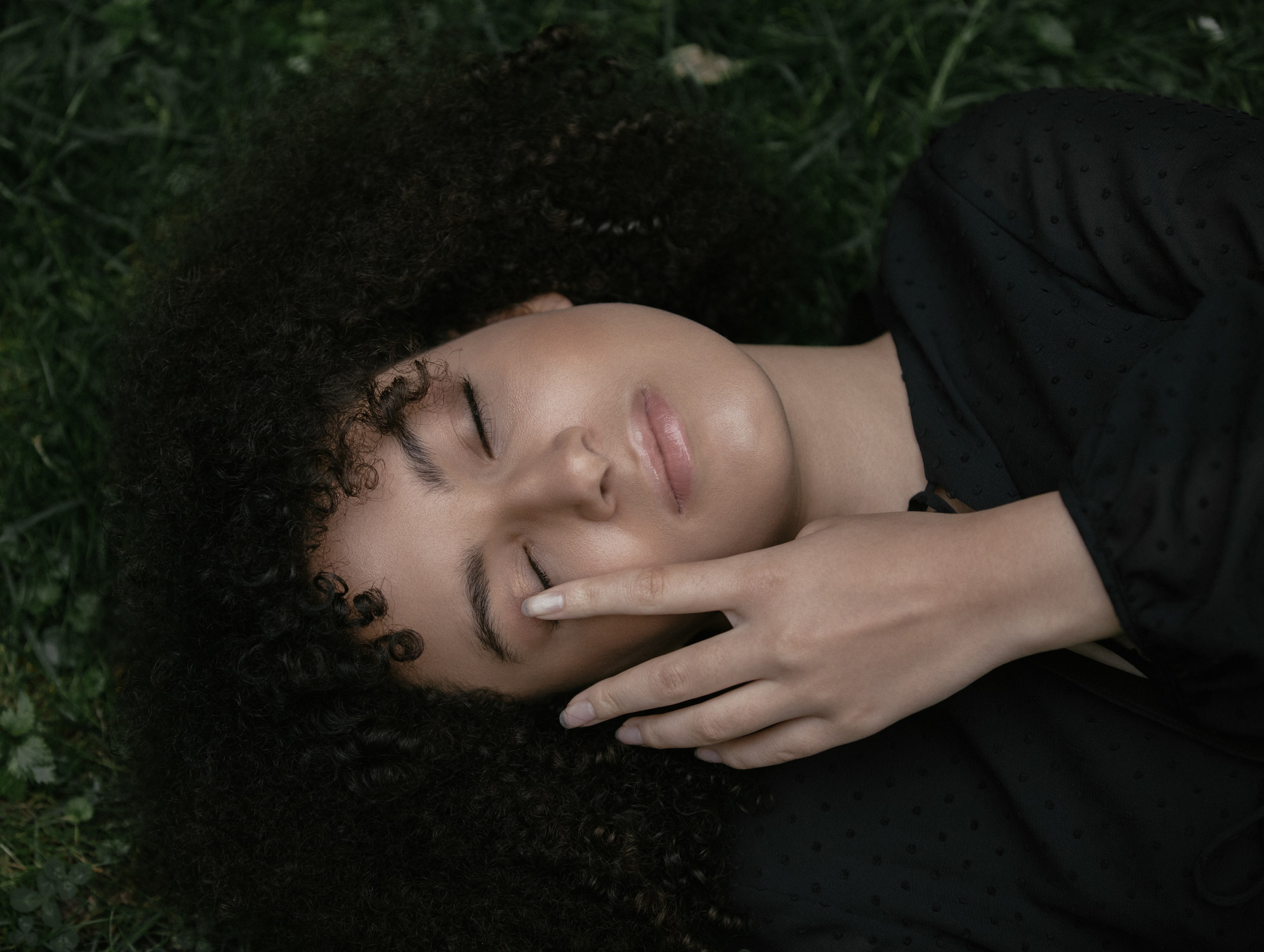 Portrait of woman lying in grass, eyes closed, hand lifted