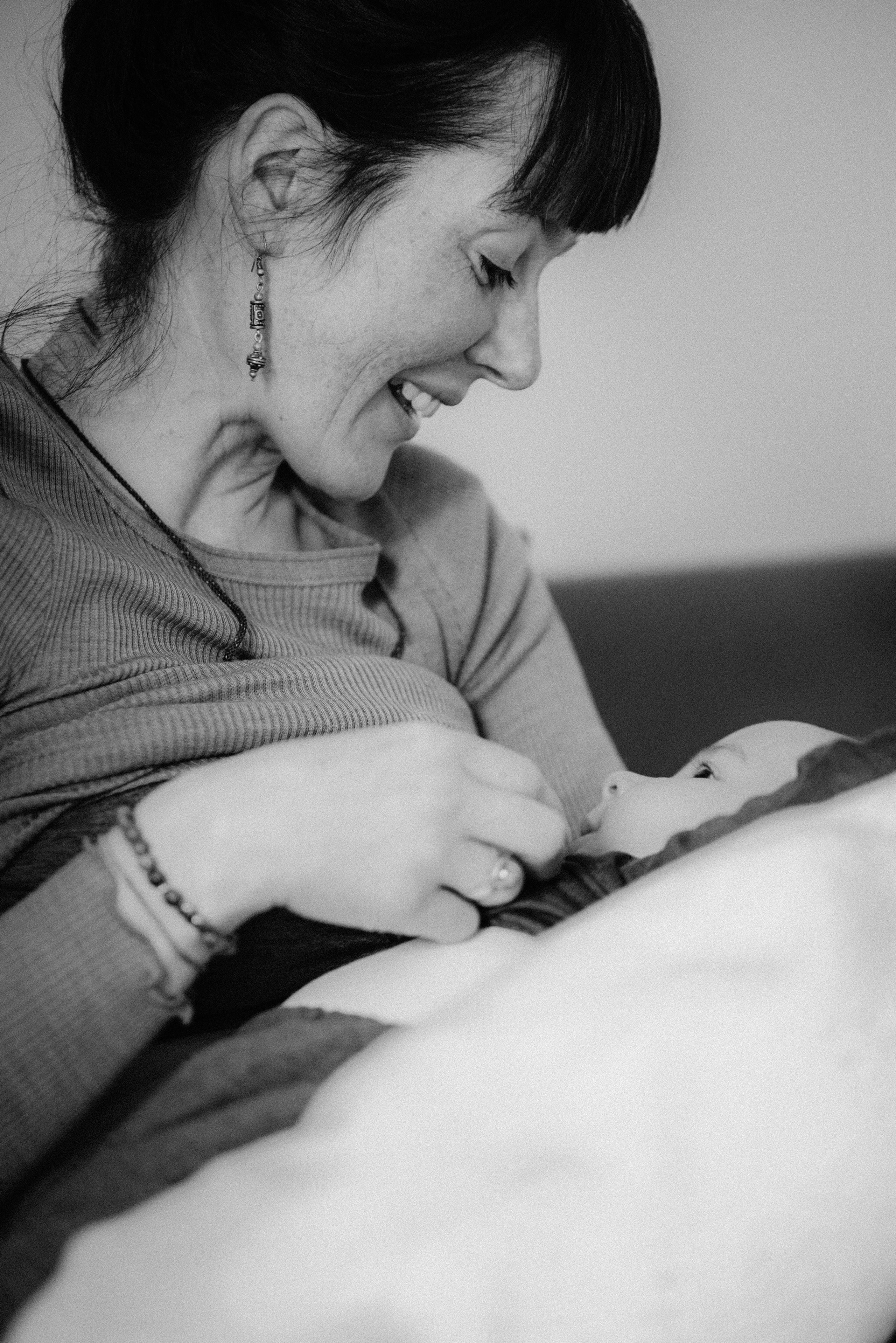 Eine Mutter mit langen Ohrringen stillt ihr Baby und lächelt es an