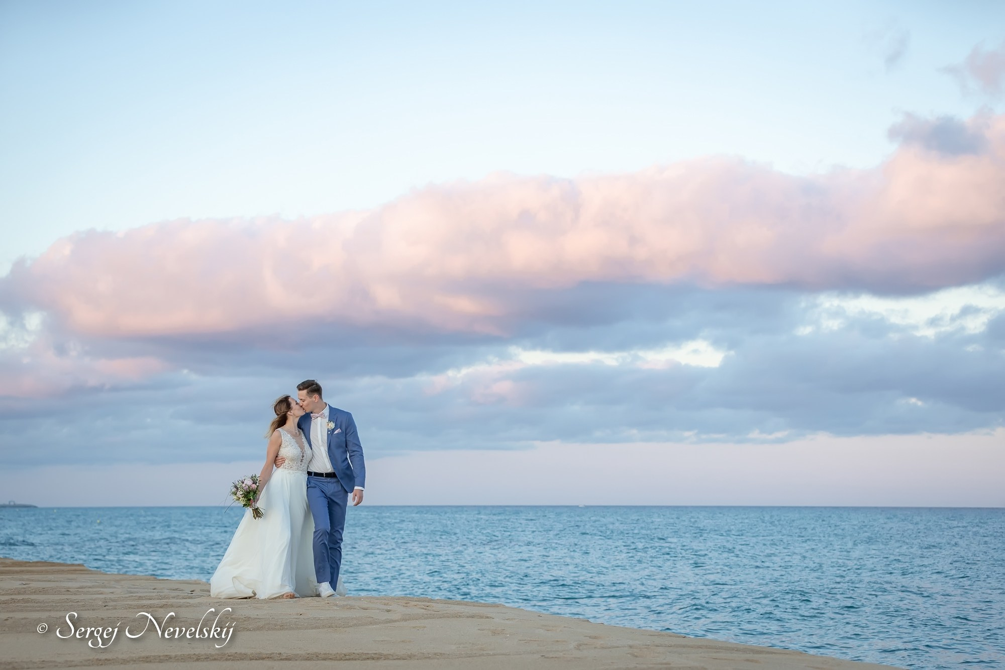 English:Newlyweds sharing a tender kiss on a cliff edge overlooking the calm sea at sunset. Bride in a flowing white lace wedding dress holding a bouquet, groom in a light blue suit with pink bow tie and boutonniere. Dramatic sky filled with soft pink and golden clouds, creating a breathtakingly romantic seaside wedding portrait. Photo by © Sergej NevelskijРусский:Молодожёны нежно целуются на краю обрыва над морем на закате. Невеста в лёгком белом кружевном свадебном платье с букетом, жених в голубом костюме с розовой бабочкой и бутоньеркой. Небо в драматичных розово-золотых облаках — невероятно романтичный морской свадебный портрет. Фото © Sergej NevelskijDeutsch:Brautpaar küsst sich zärtlich am Klippenrand mit Blick aufs Meer beim Sonnenuntergang. Braut in einem fließenden weißen Spitzenbrautkleid mit Brautstrauß, Bräutigam im hellblauen Anzug mit rosa Fliege und Ansteckblume. Dramatisch rosa-goldener Wolkenhimmel – ein atemberaubend romantisches Hochzeitsporträt am Meer. Foto © Sergej Nevelskij
