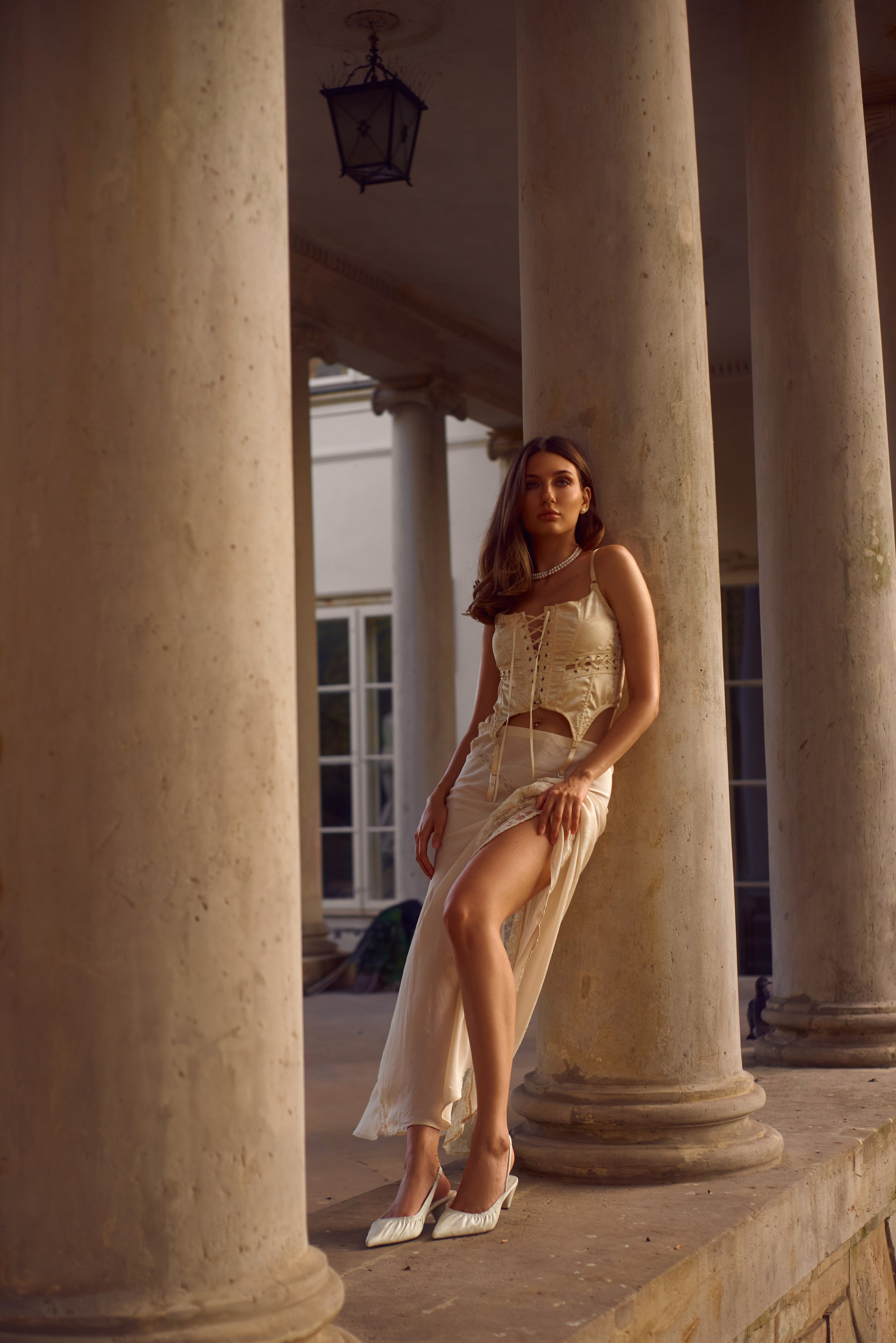 Таємнича краса архітектури – Жінка у легкому вбранні з відкритою спиною стоїть серед величних колон, дозволяючи світлу й тіням створити драматичну композицію.
