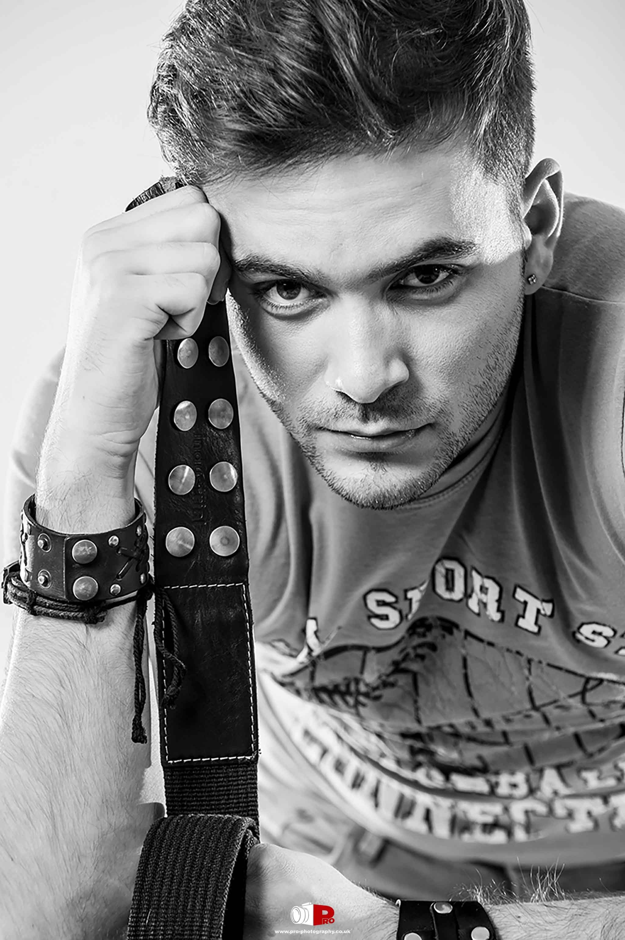 Intense close-up black and white portrait of a man holding a leather-studded belt, exuding a strong and confident look.