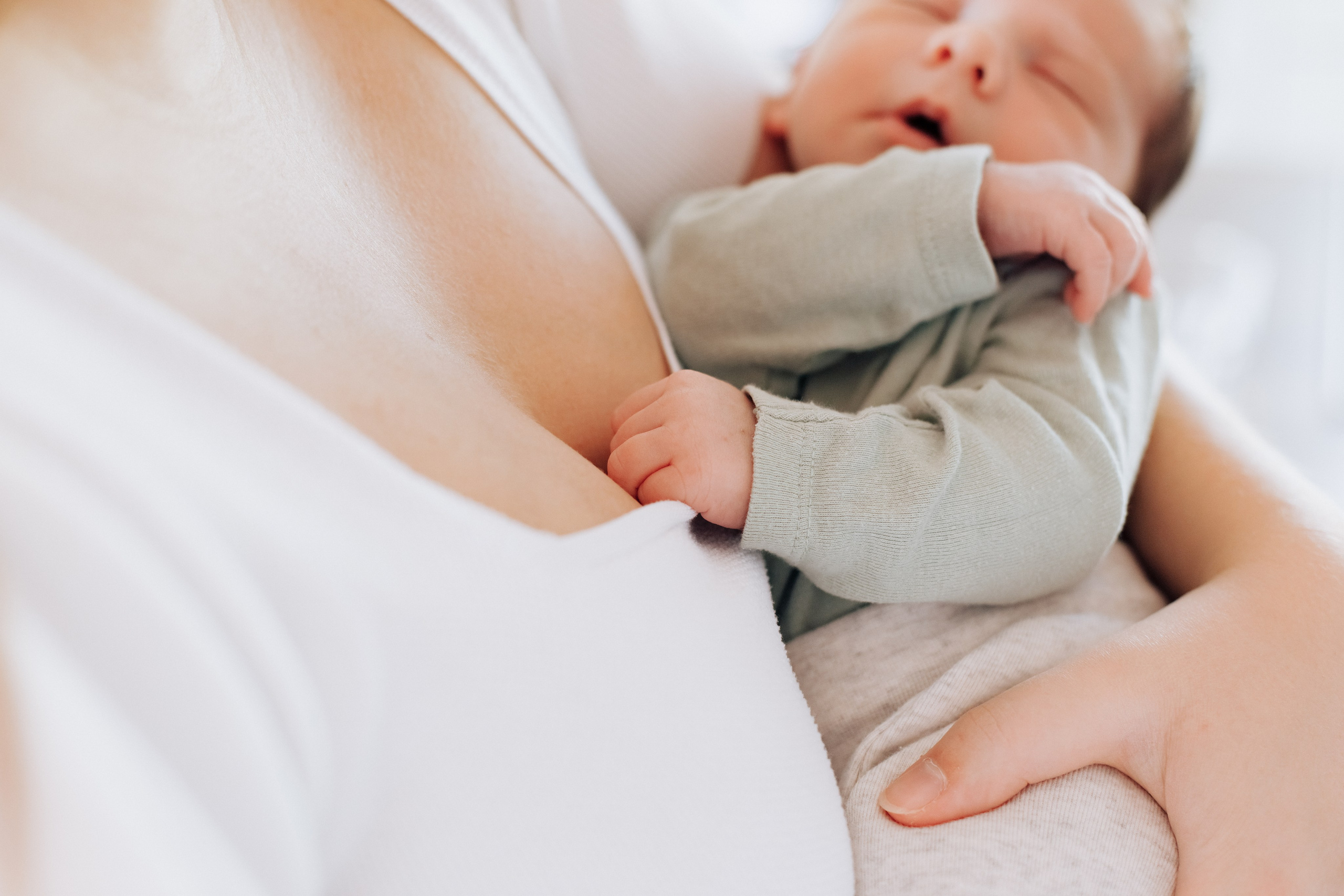Ein Baby hält mit seiner kleinen Hand an dem T-Shirt der Mutter. Ein süßer und liebevoller Moment.