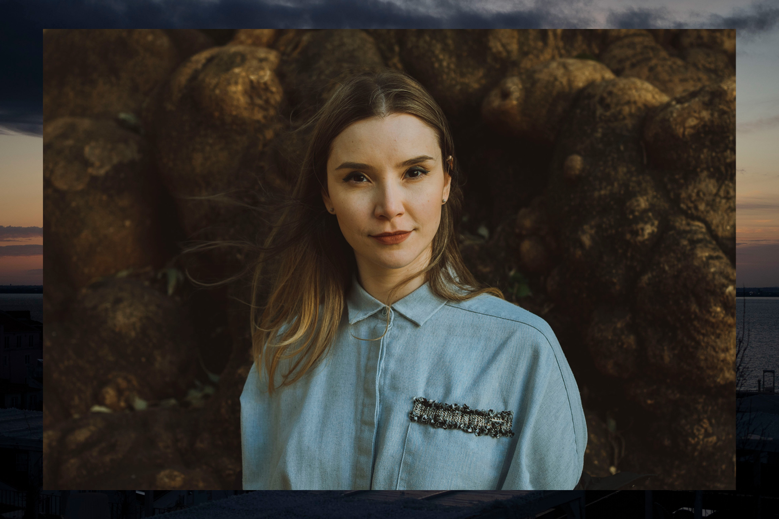 A front portrait of a young woman with long hair on a dark background. The woman is wearing a blue blouse. 