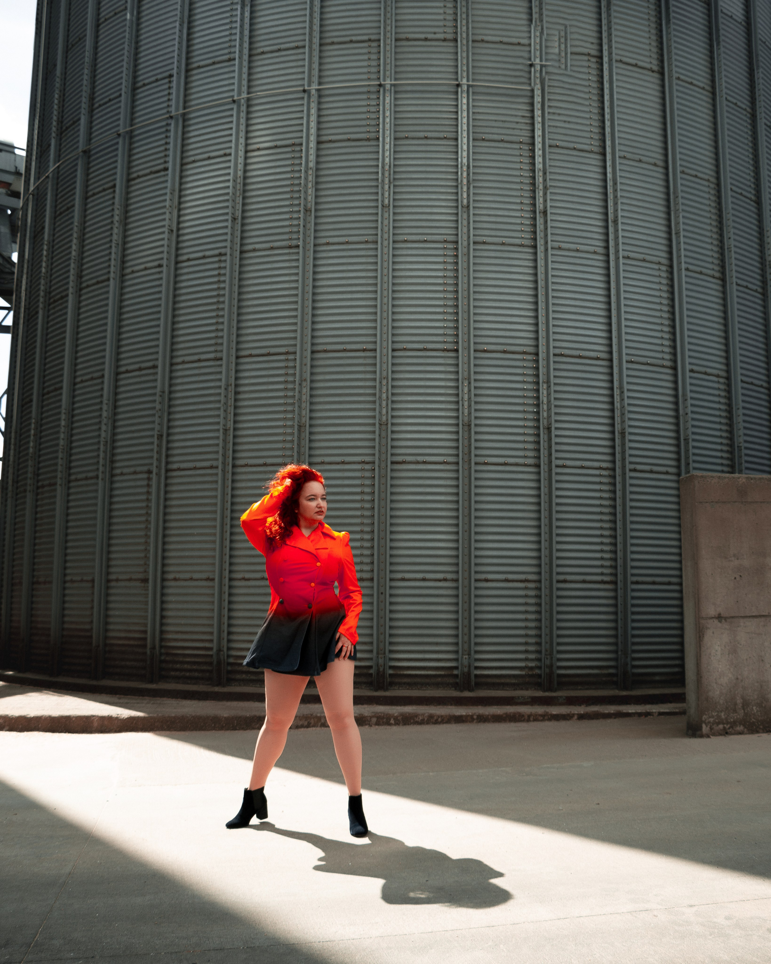 Starkes Portrait einer Frau mit roten Haaren und rotem Kleid auf einem Fabrikgelände
