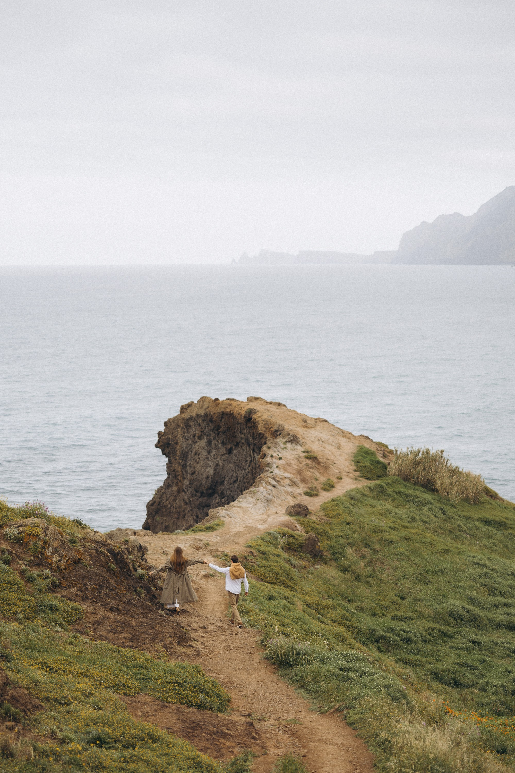 Beautiful engagement moment by the ocean in Madeira, Portugal, as one partner kneels to propose while waves crash in the background