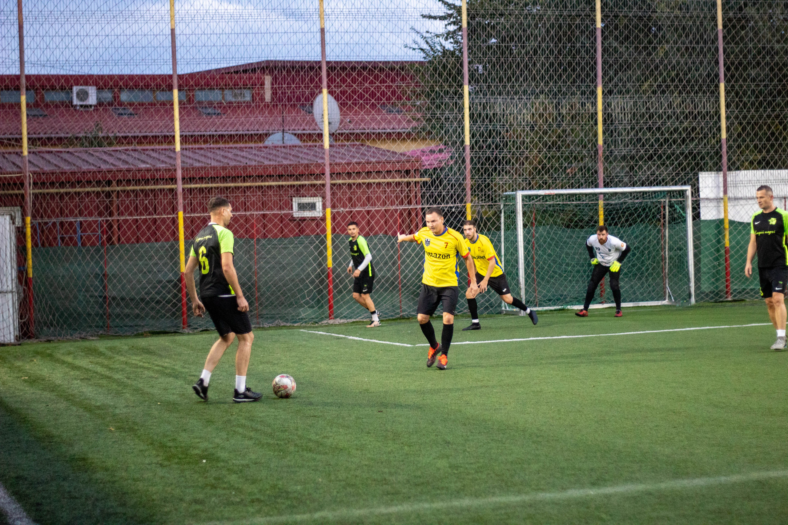 Football players chasing the ball during an evening match on a turf field.