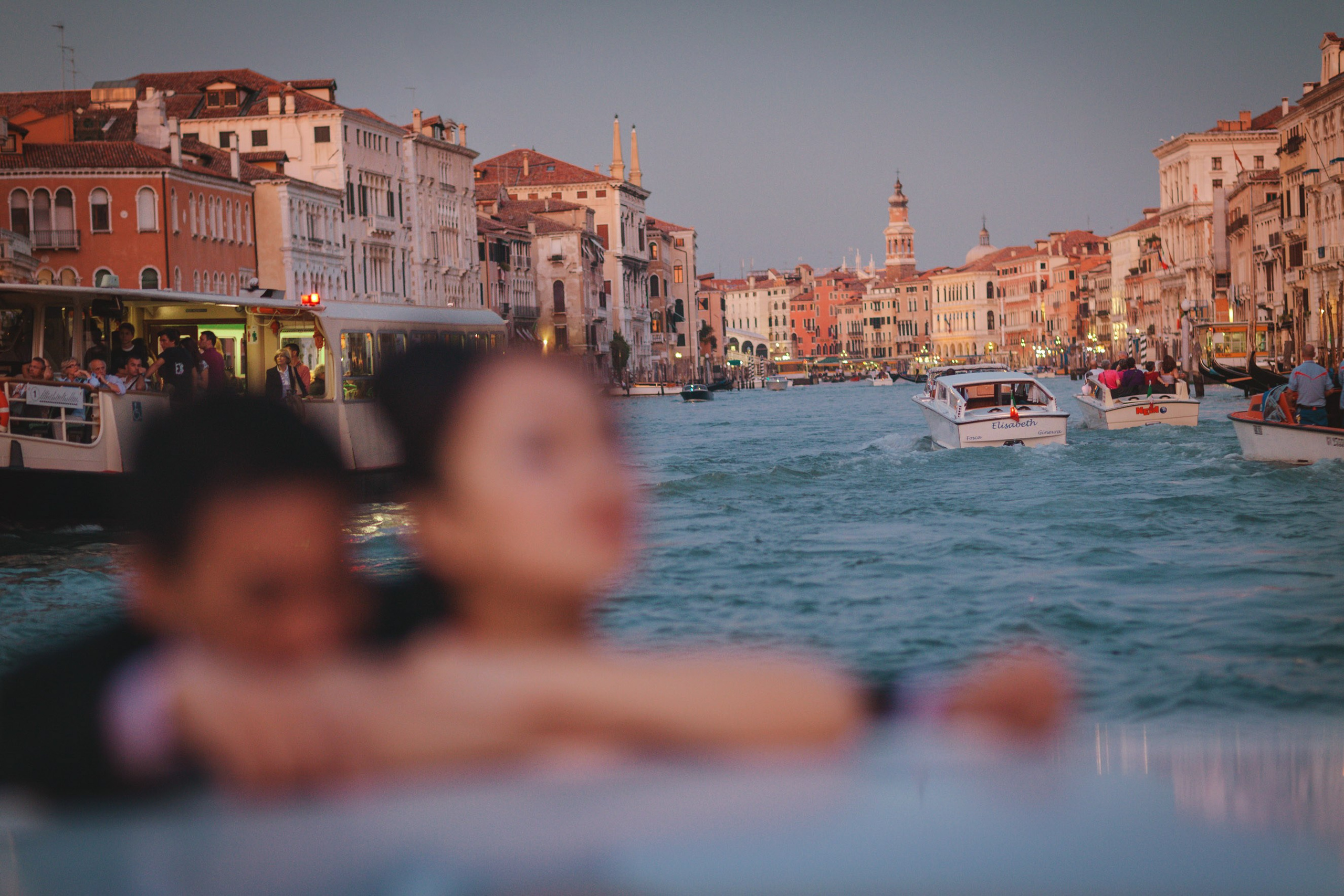 An elegantly dresed young Thai couple enjoy the atmosphere of Venice aboard a private boat at dusk.