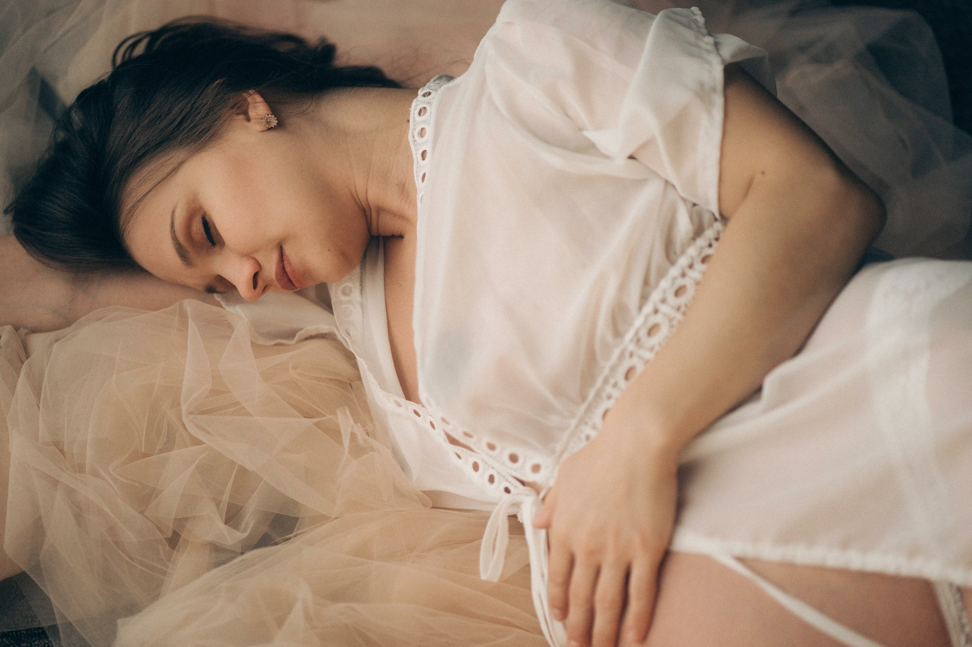 Съемка беременности в студии — будущая мама в светлом платье лежит на кровати, атмосферный портрет