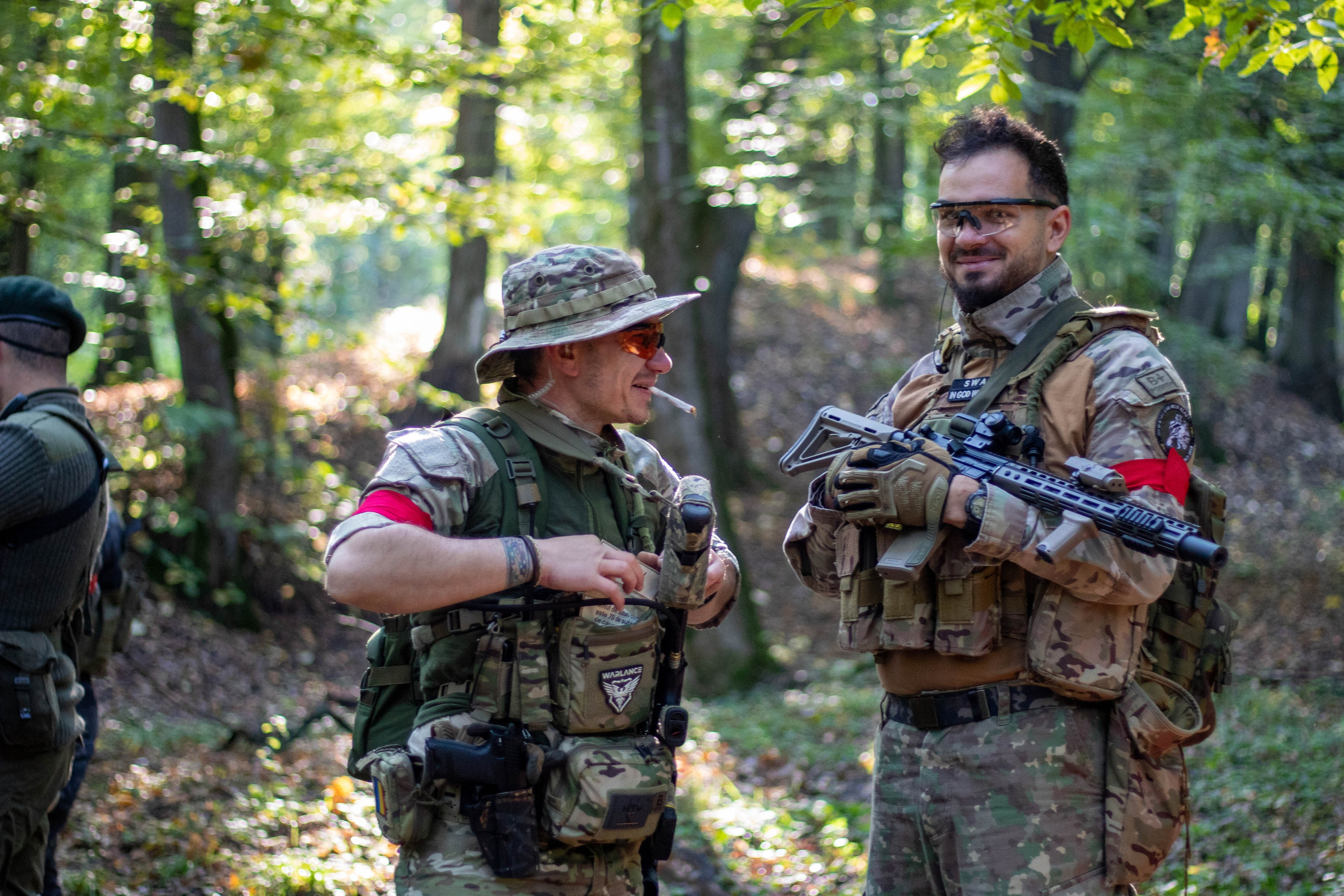 Two airsoft players posing with rifles and camo in the woods during a match break.